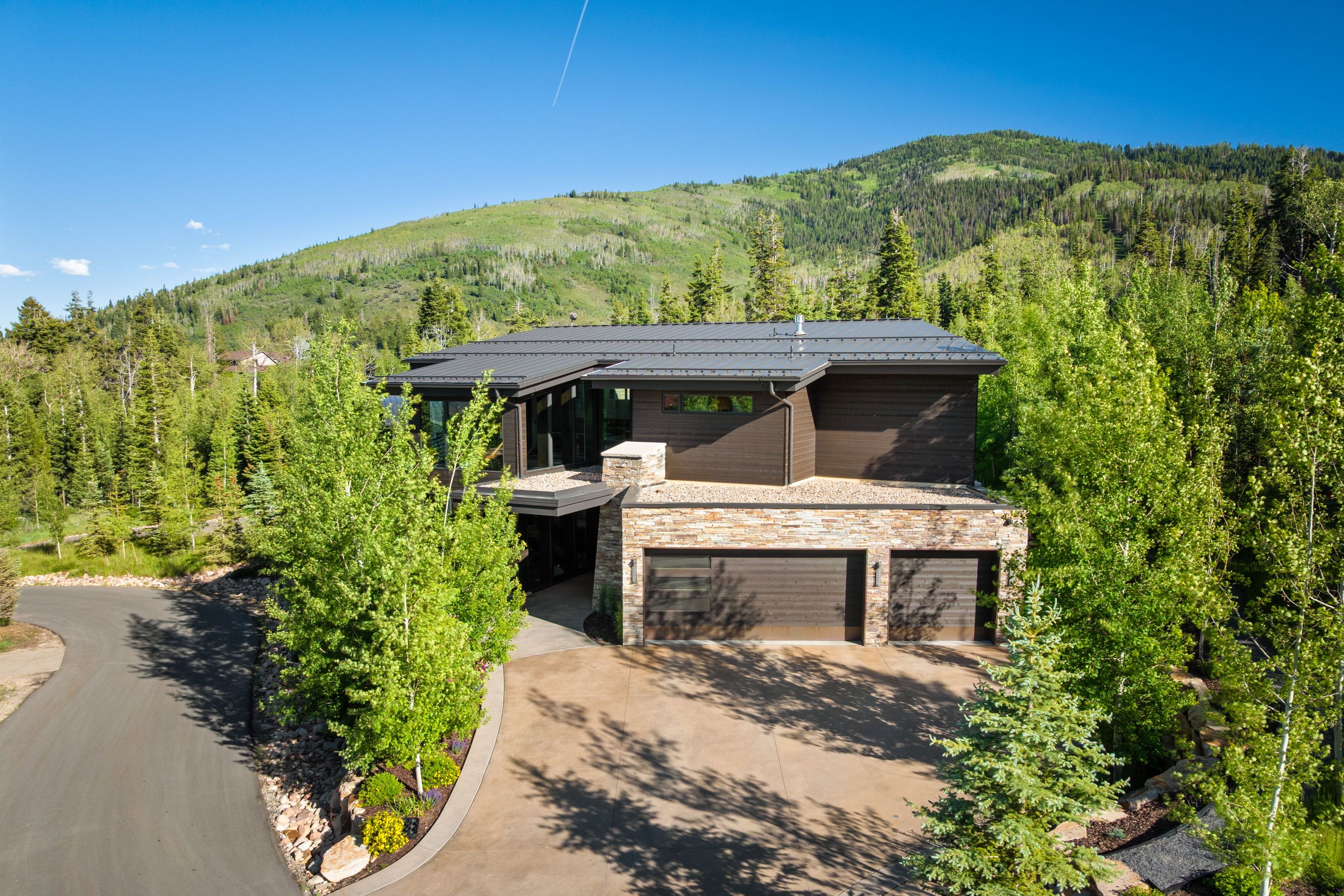 Modern mountain residence featuring a stone-clad lower level, dark siding, and a metal roof