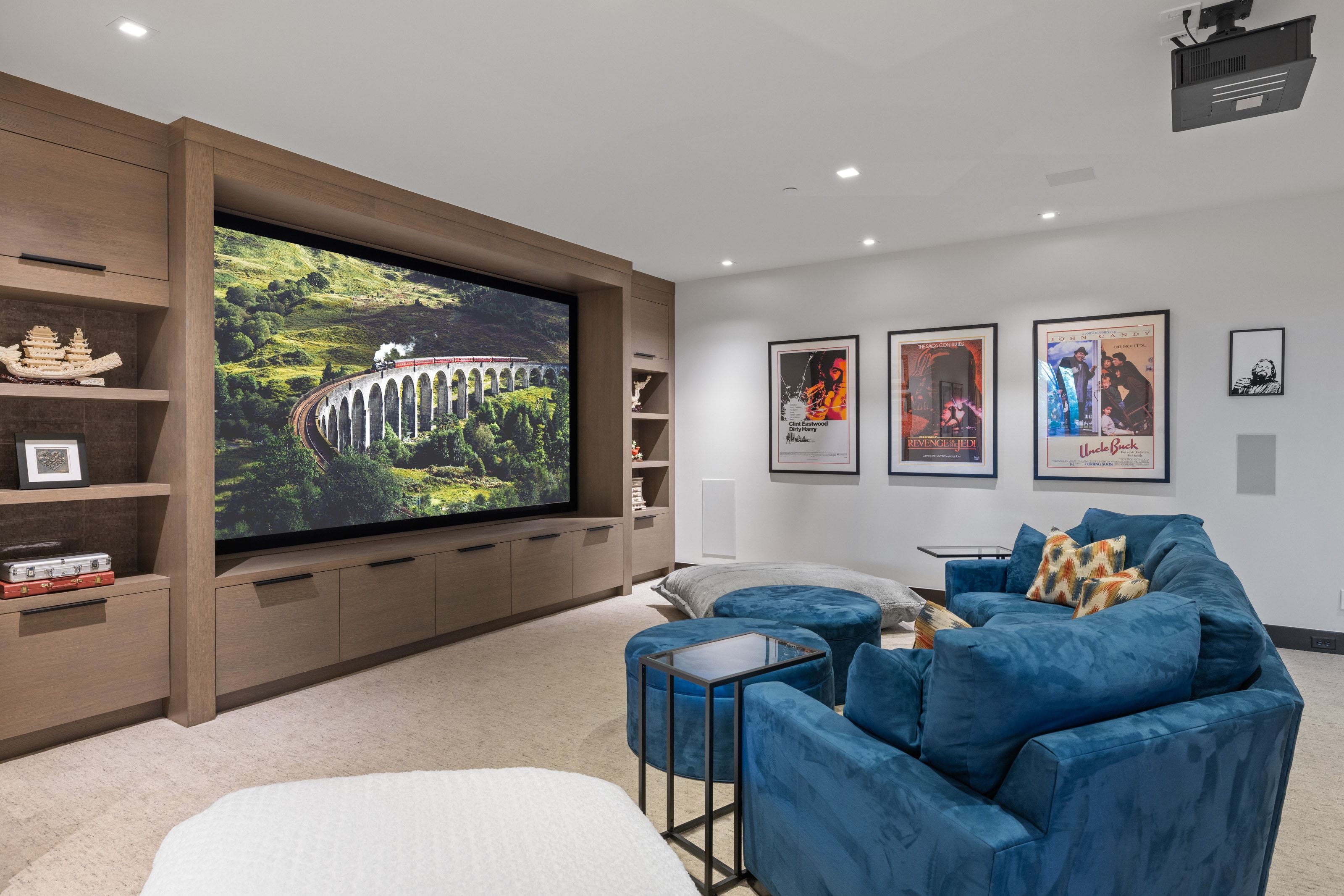 Home theater featuring a large projection screen, built-in cabinetry with open shelving, recessed lighting, and integrated ceiling-mounted projector