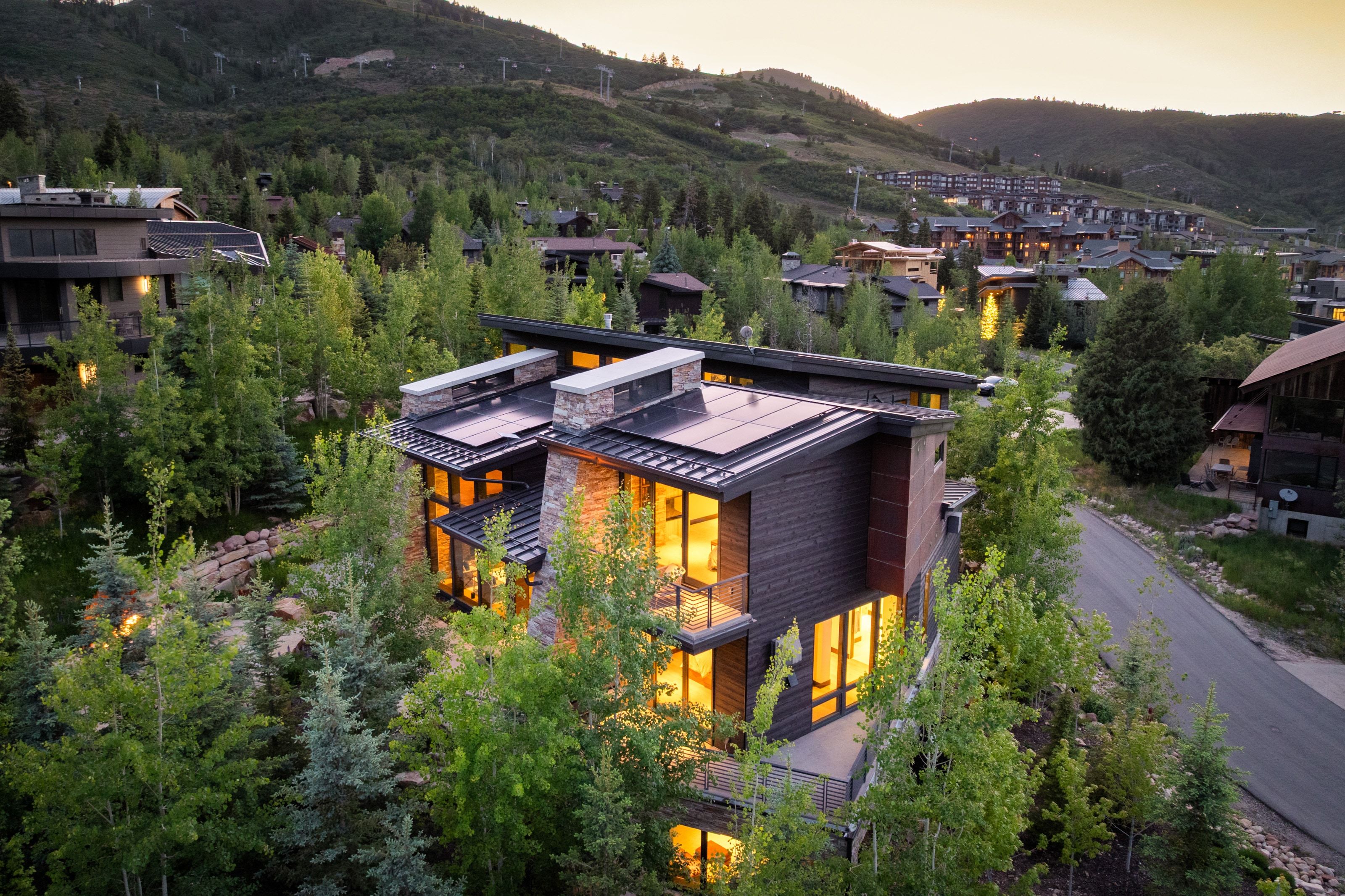 Modern multi-level residence featuring expansive window walls, stone accents, and dark wood-finish siding