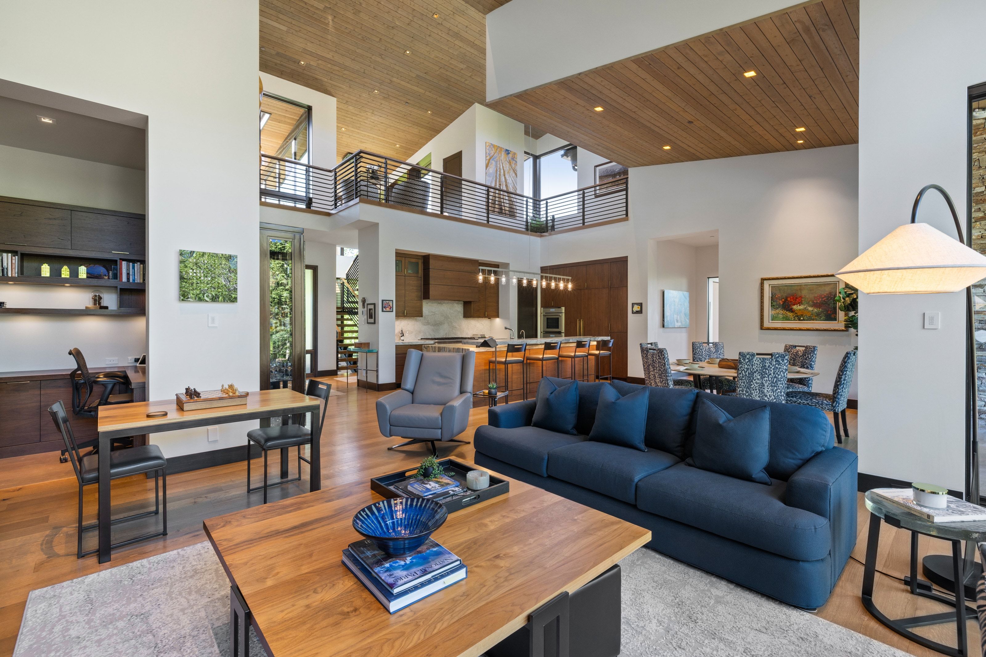 Expansive open-concept living area featuring a vaulted wood-finish ceiling, hardwood flooring, and a two-story layout with an upper-level balcony