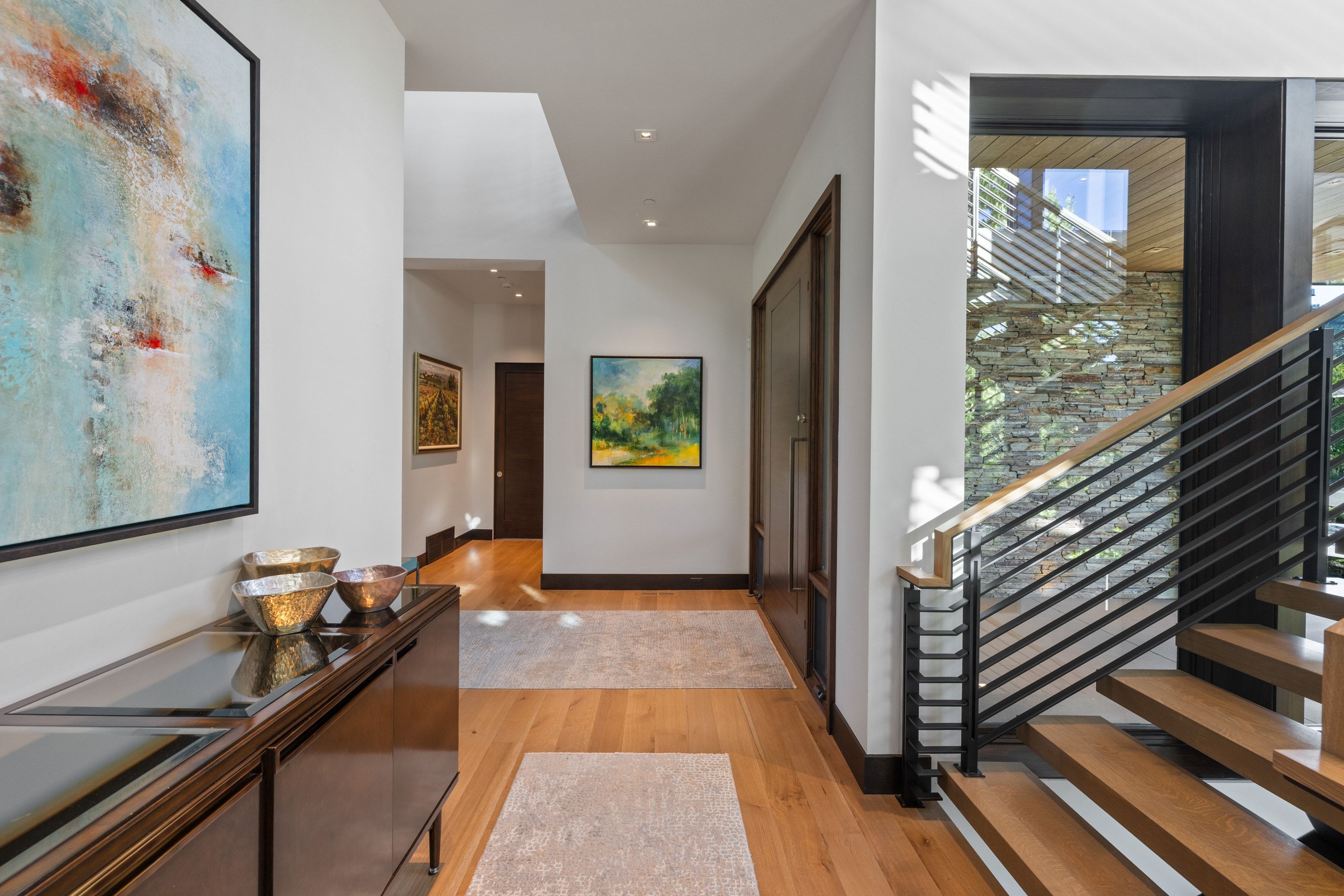 Floating wood-finish staircase with contemporary metal railing, stone accent wall, and recessed lighting