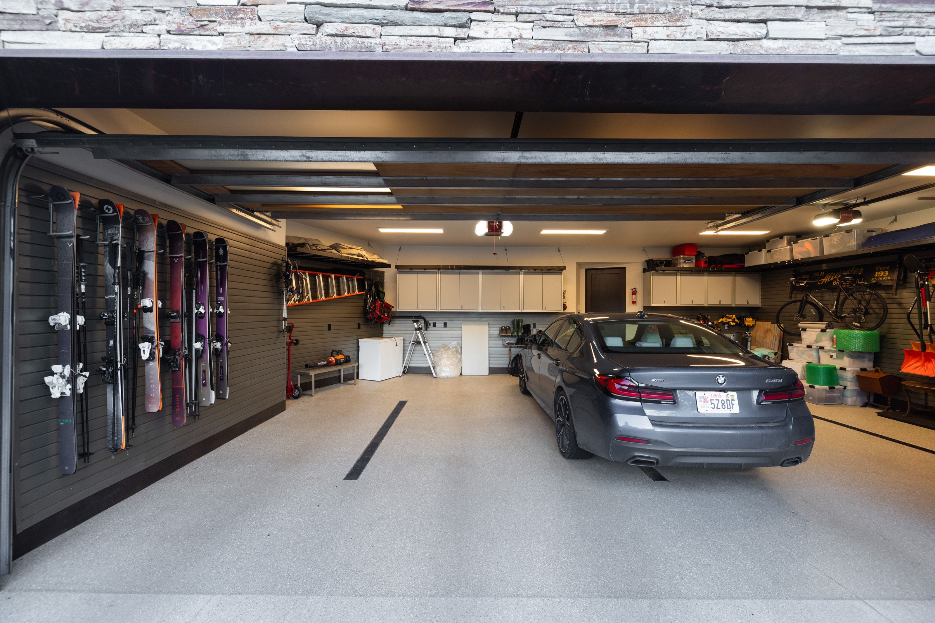 Spacious garage featuring a durable epoxy floor, integrated wall storage systems, extensive overhead lighting, and built-in cabinetry