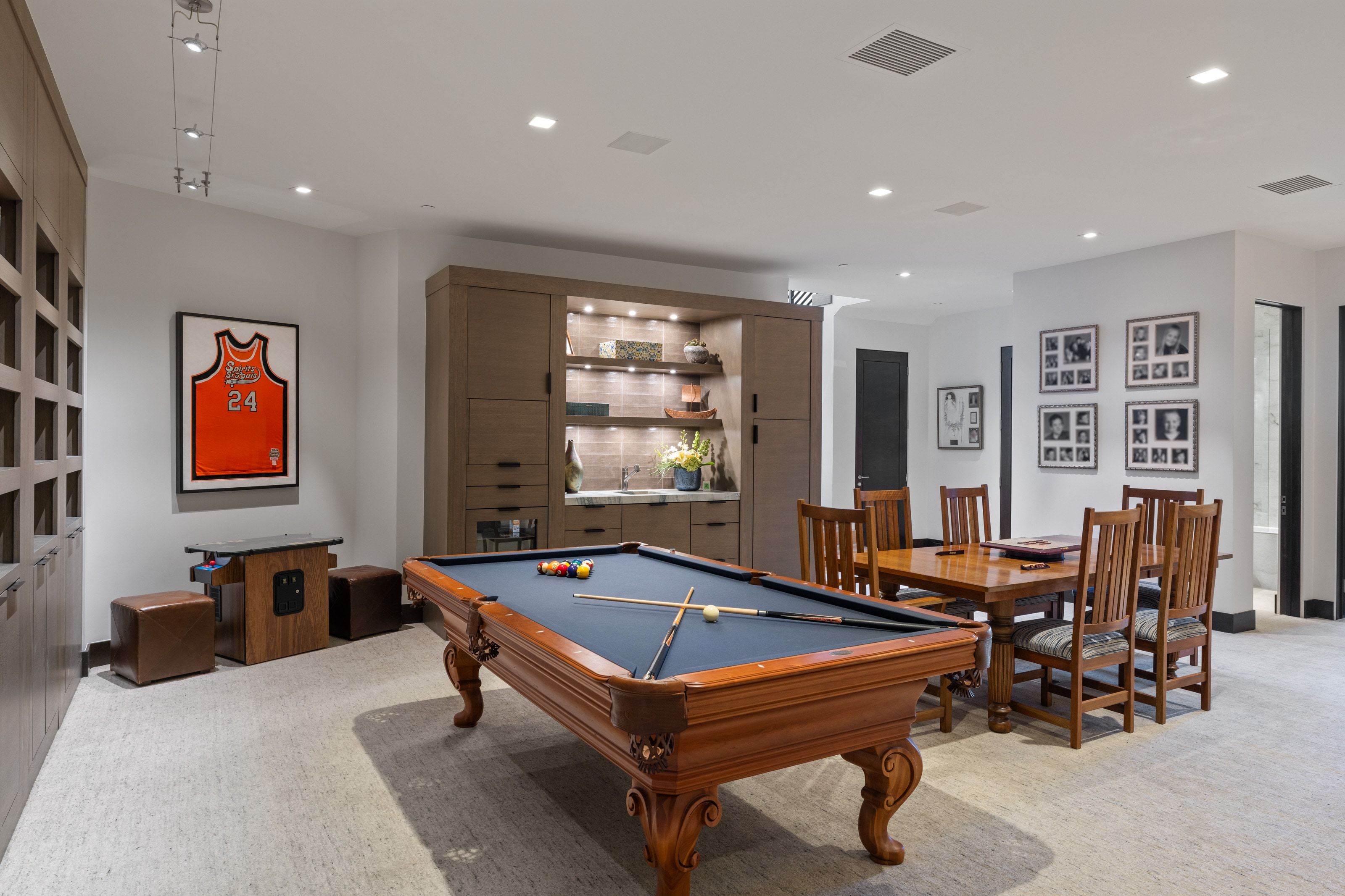 Spacious entertainment room featuring a wood-finish billiards table, integrated wet bar with recessed lighting, and a dedicated dining table with seating