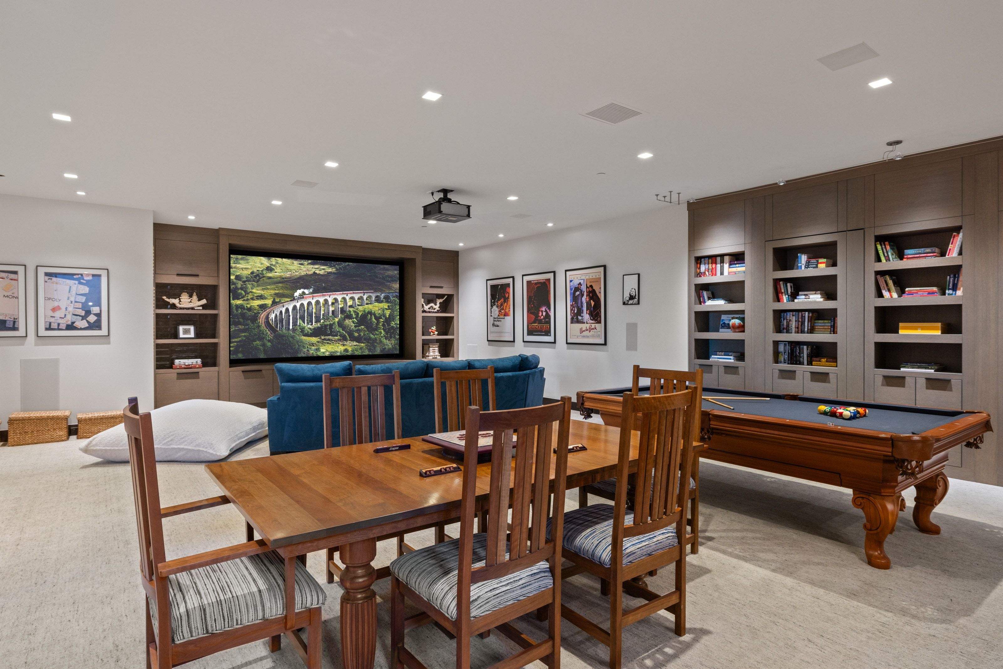 Spacious entertainment room featuring a large projection screen with built-in media cabinetry, a billiards table, recessed lighting, and wall-mounted shelving
