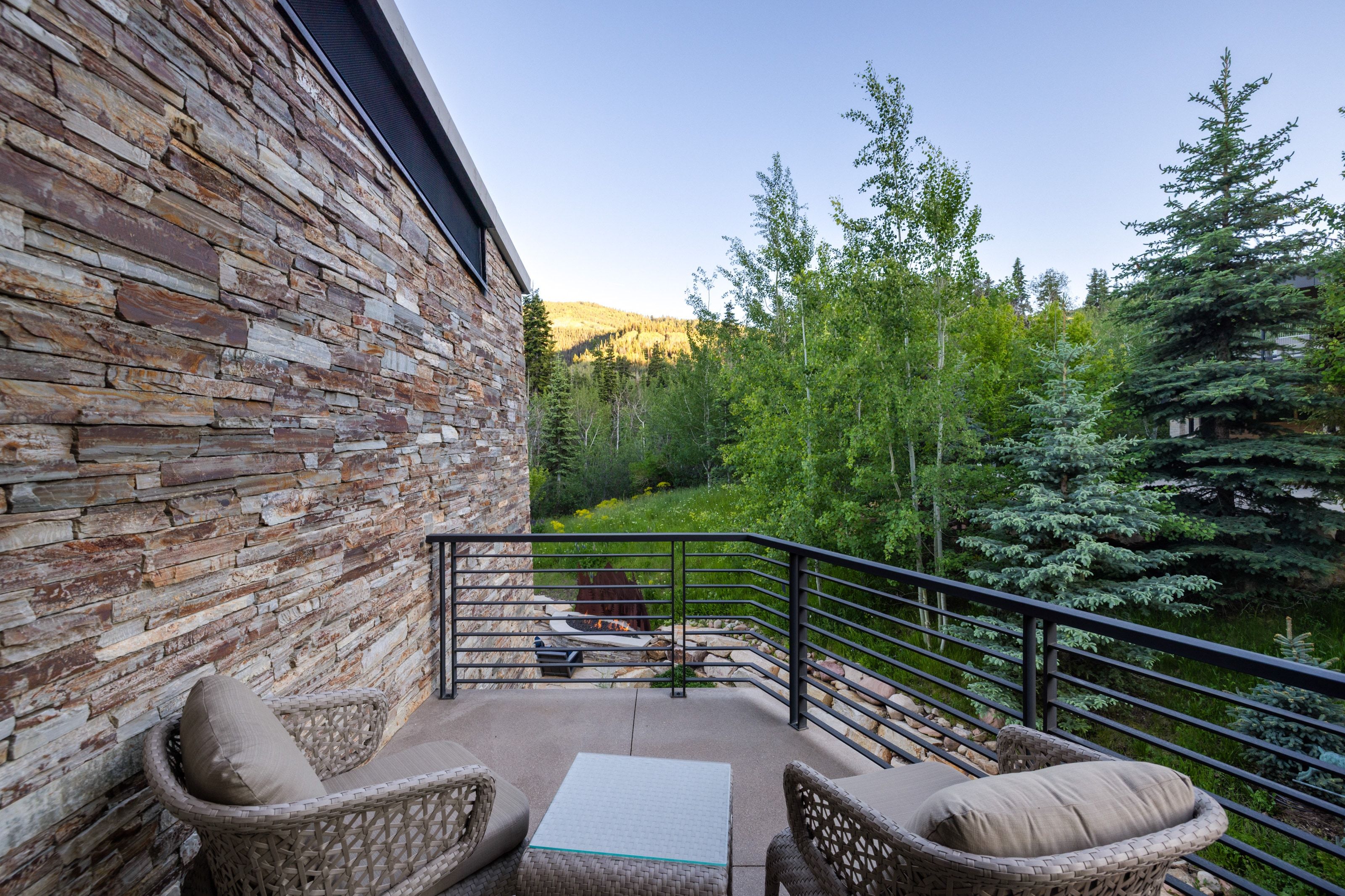 Outdoor patio featuring a stone veneer exterior, black metal railing, and concrete flooring
