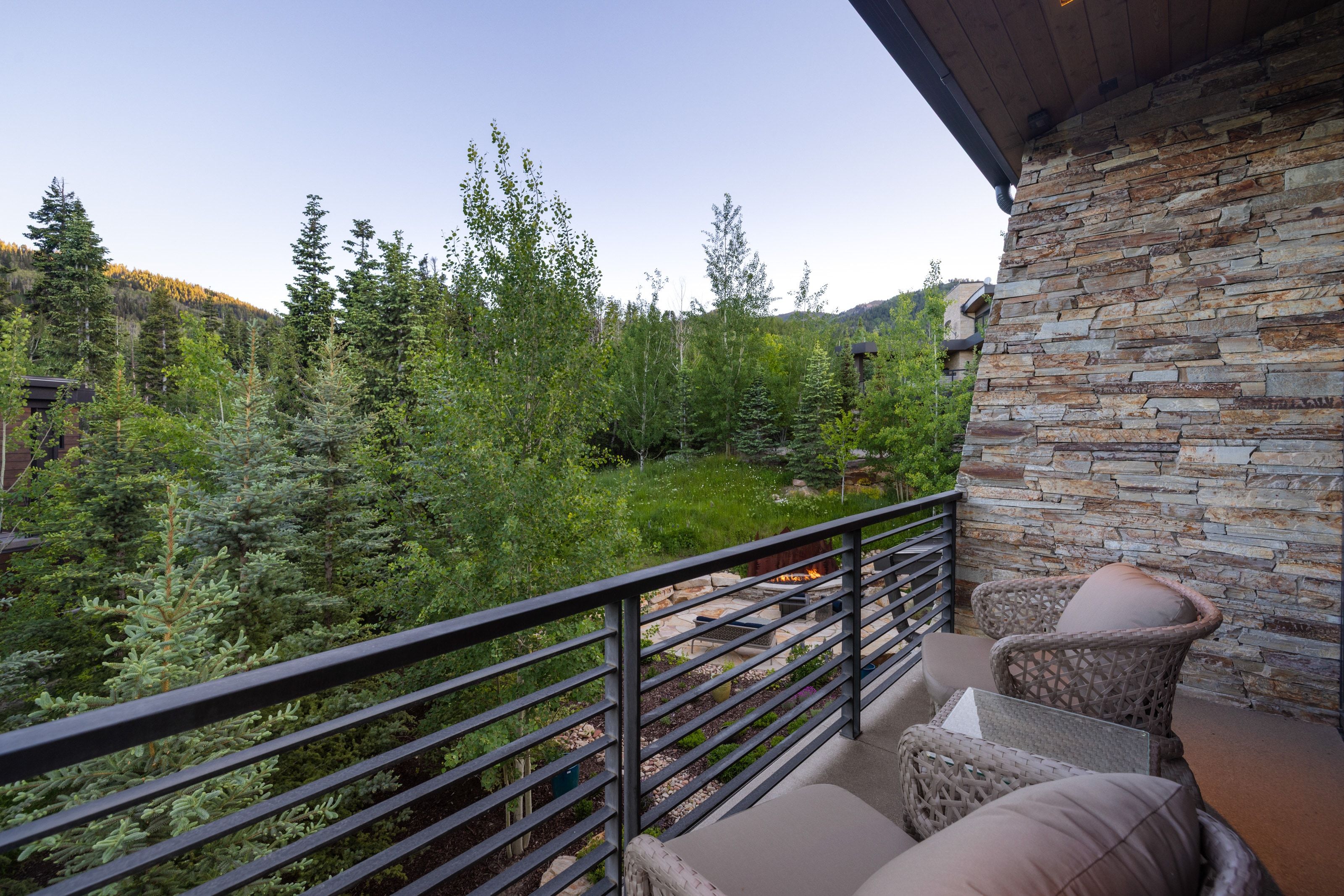 Private balcony with stone veneer exterior wall and horizontal metal railings overlooking mature trees and natural landscaping