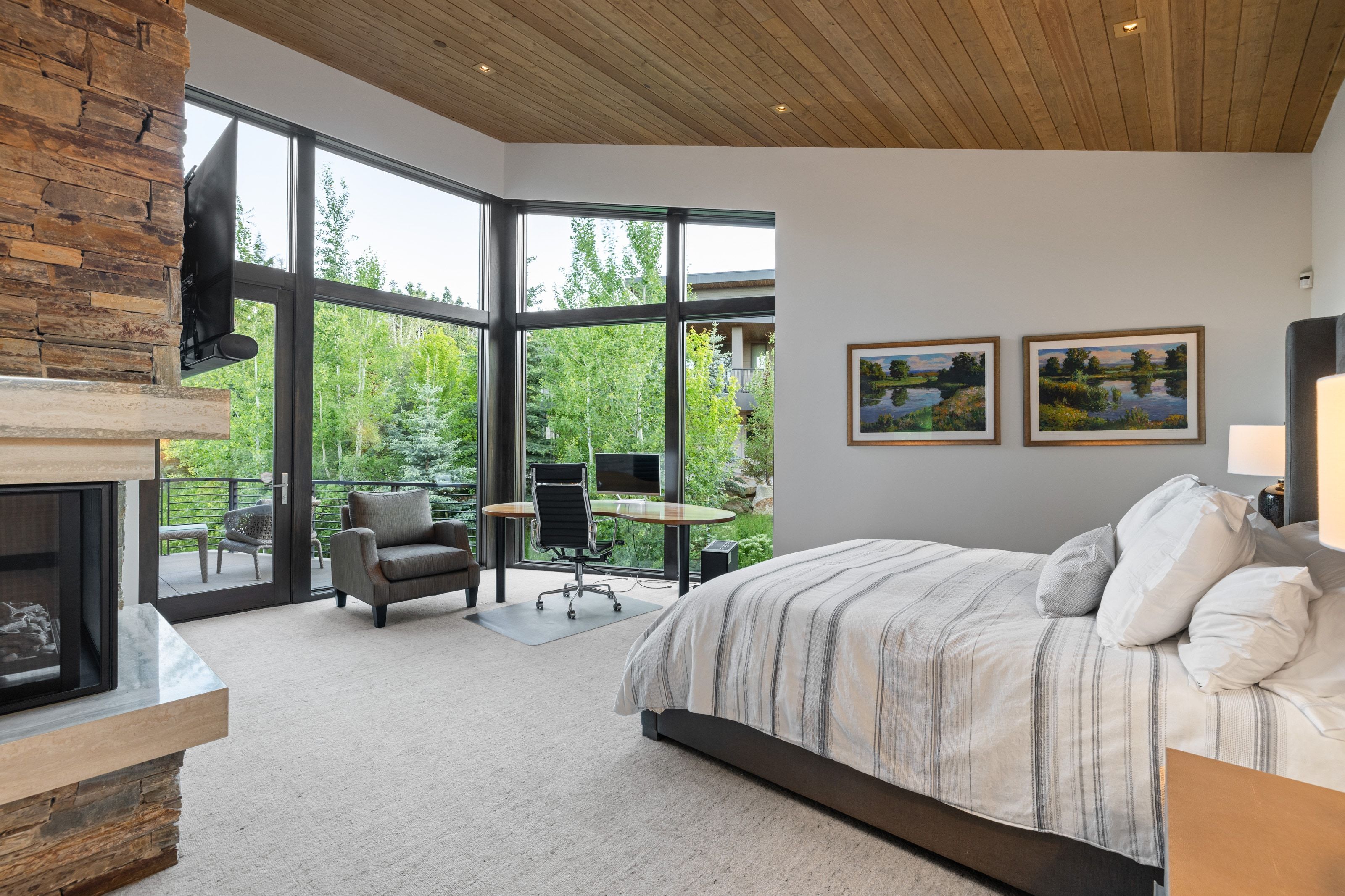 Interior space featuring a stone-clad fireplace with a light-colored mantel, expansive floor-to-ceiling windows, and a wood-slat ceiling with recessed lighting