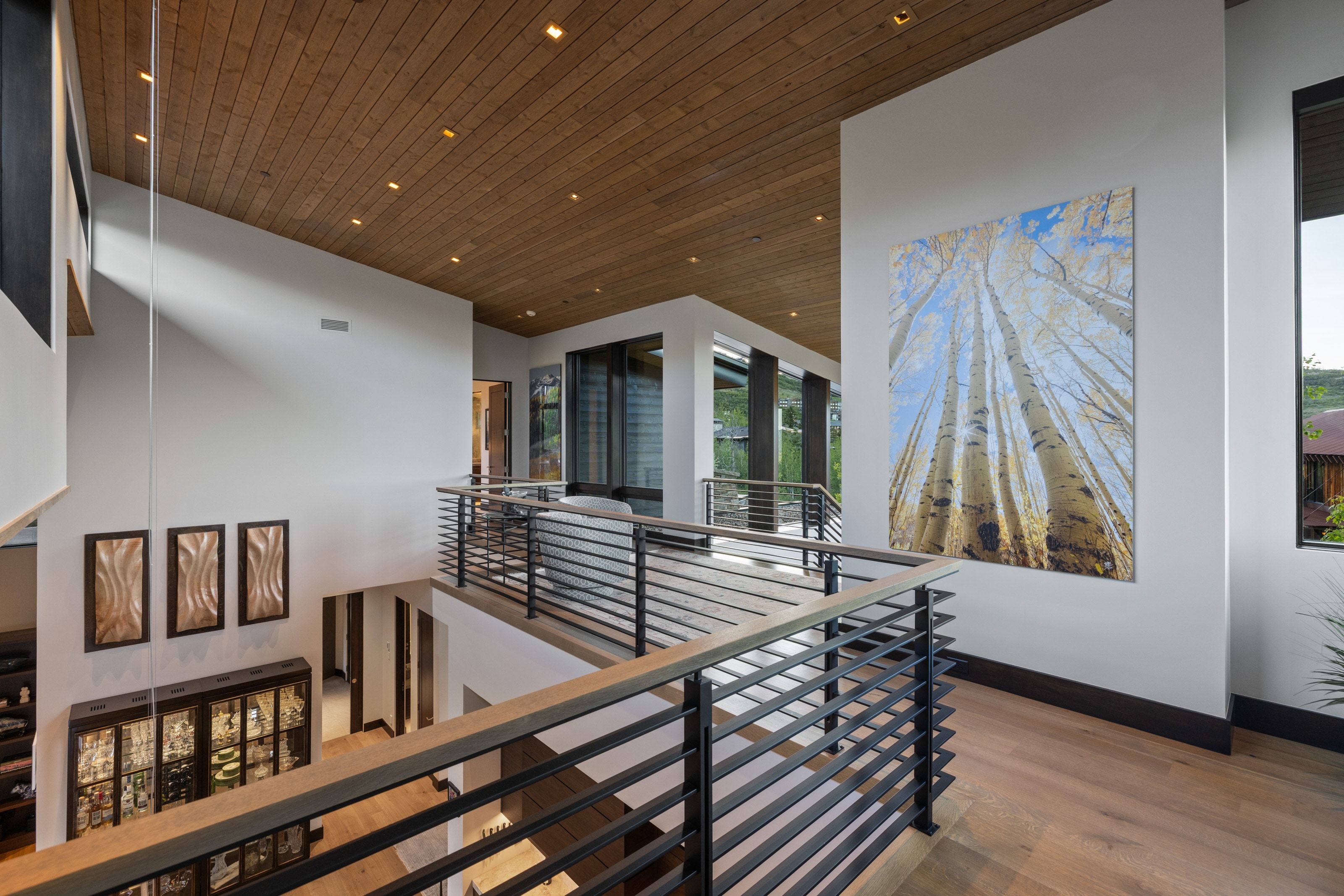 Multilevel interior featuring wood-finish flooring, a wood-paneled ceiling with recessed lighting, and modern horizontal bar railings