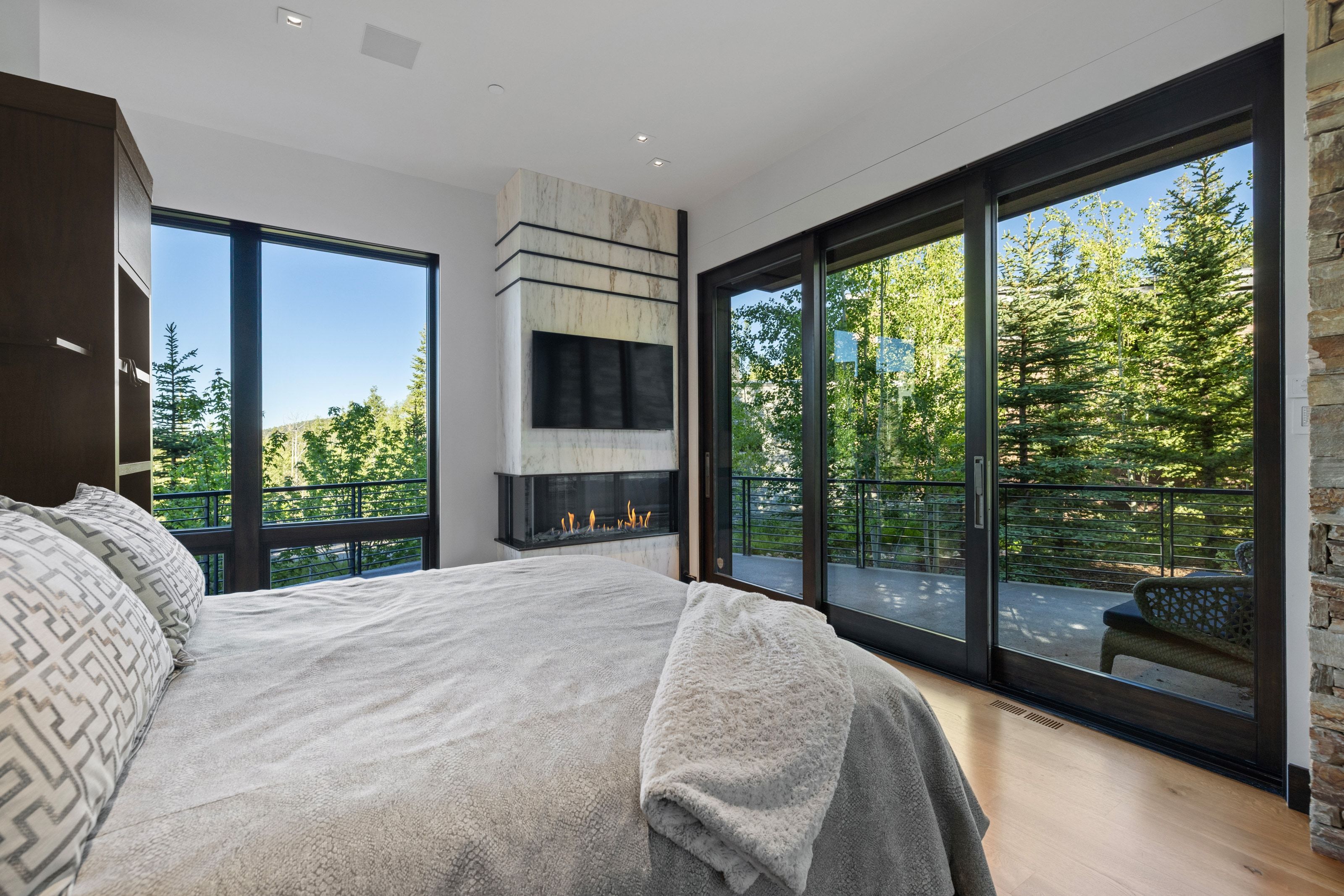 Spacious room featuring floor-to-ceiling windows and sliding glass doors, a built-in linear fireplace with a stone surround, wood-finish flooring, and a built-in dark wood cabinet
