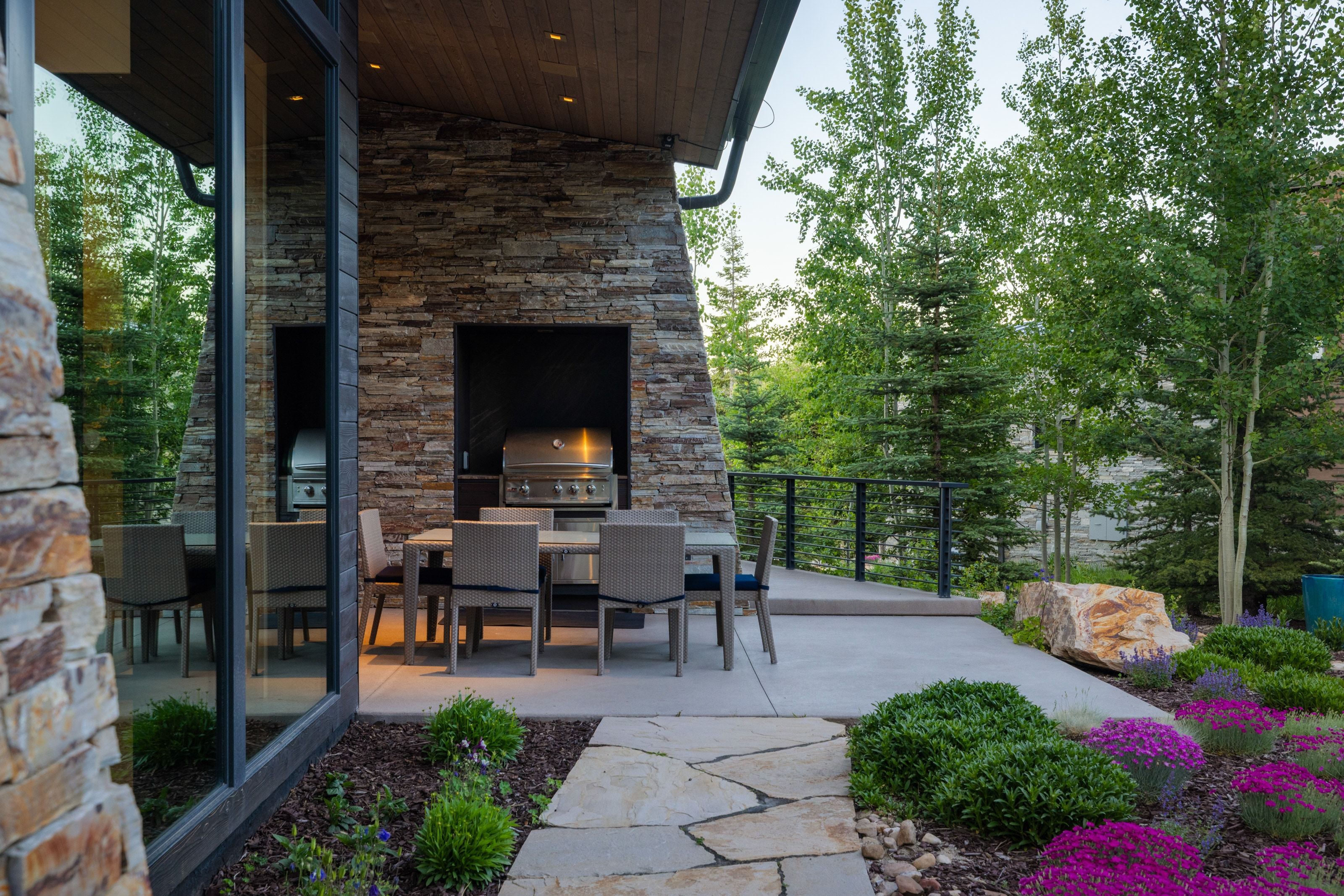 Outdoor living space featuring a built-in grill station with stone surround, concrete patio, and mature landscaping