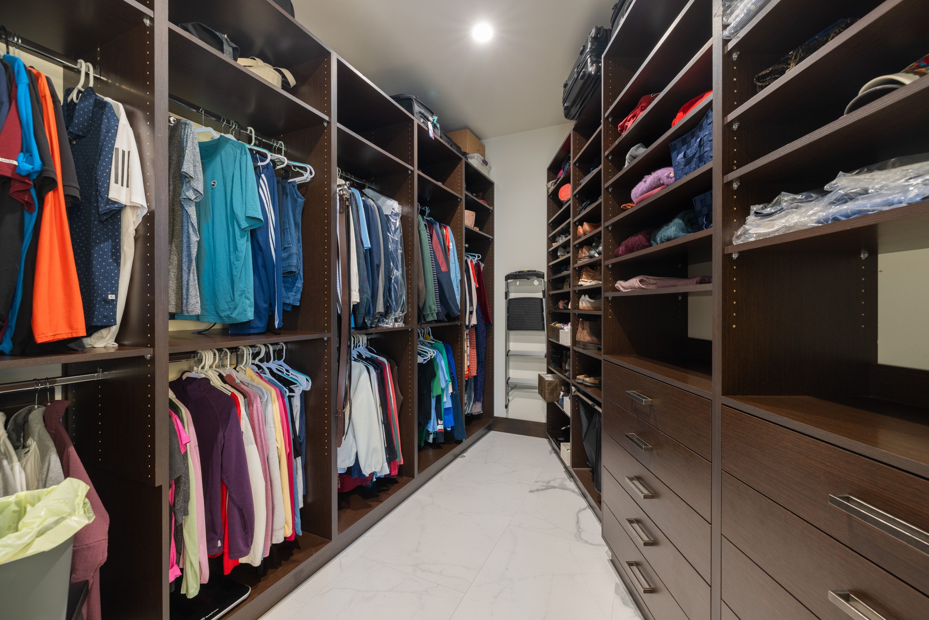 Spacious custom closet featuring dark wood-finish cabinetry, integrated shelving, and multiple hanging rods