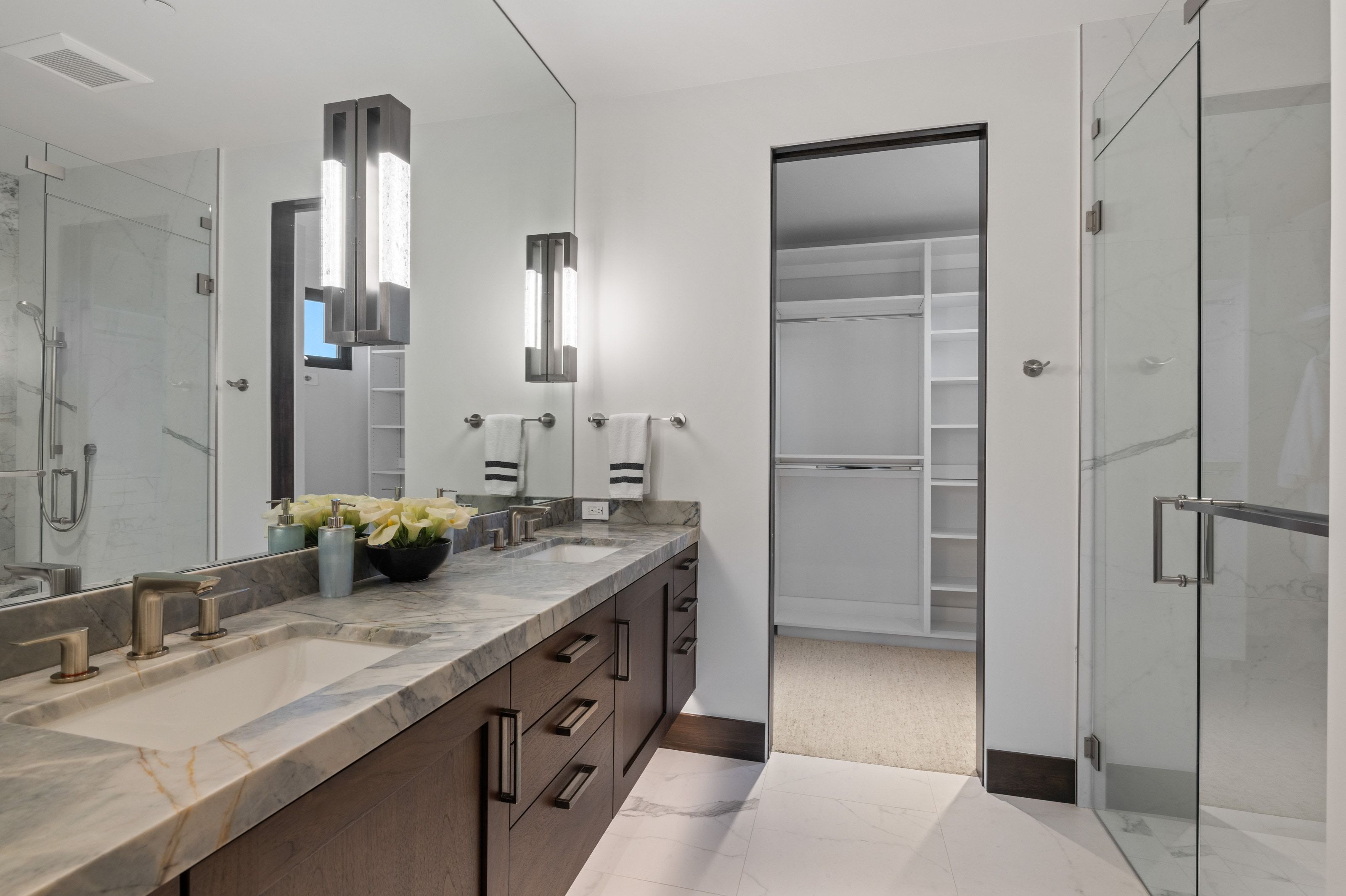 Dual sink vanity with stone countertop, dark wood-finish cabinetry, and contemporary wall sconces