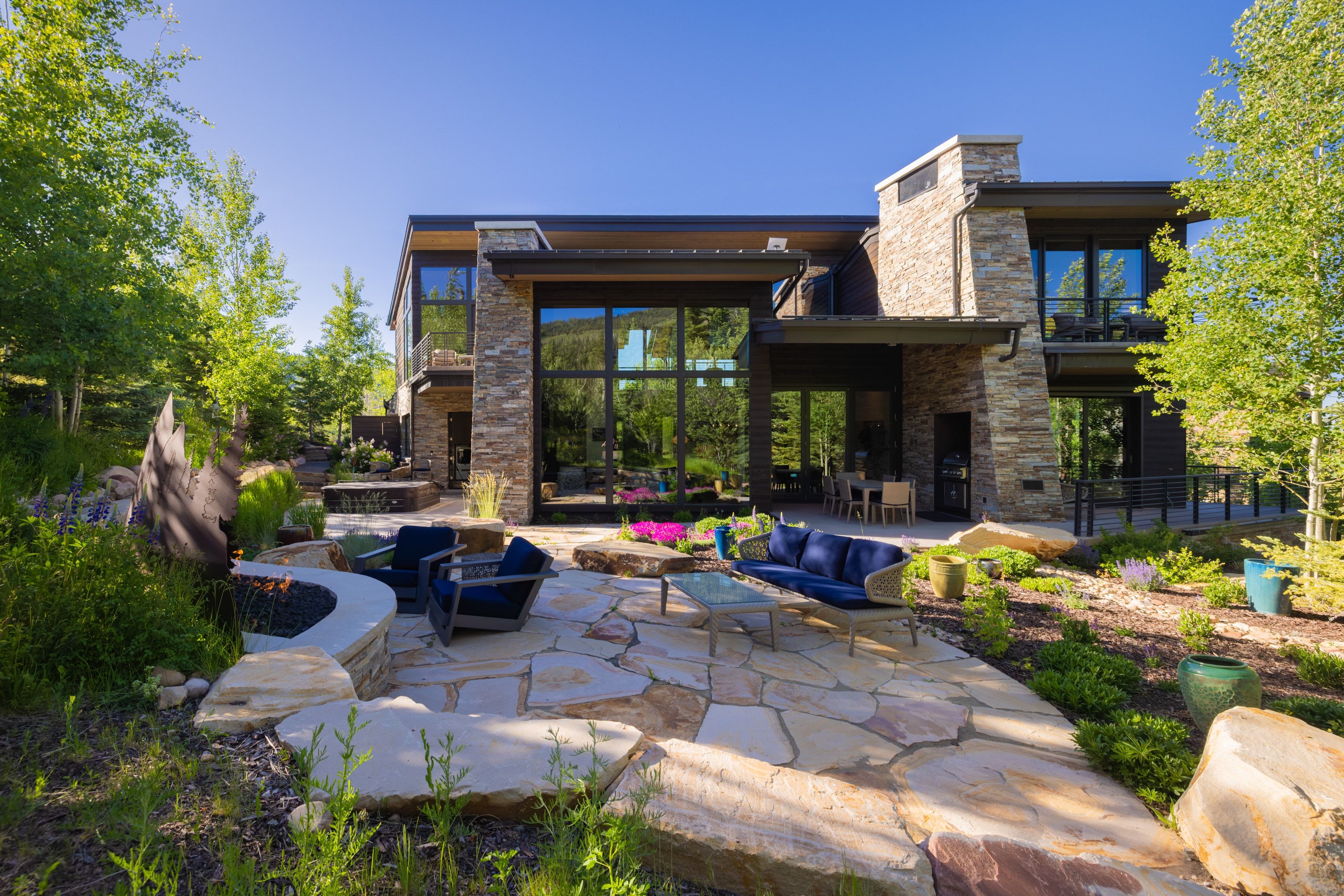 Exterior featuring a natural stone facade, extensive multi-level flagstone patio, built-in fire pit, and expansive glass doors