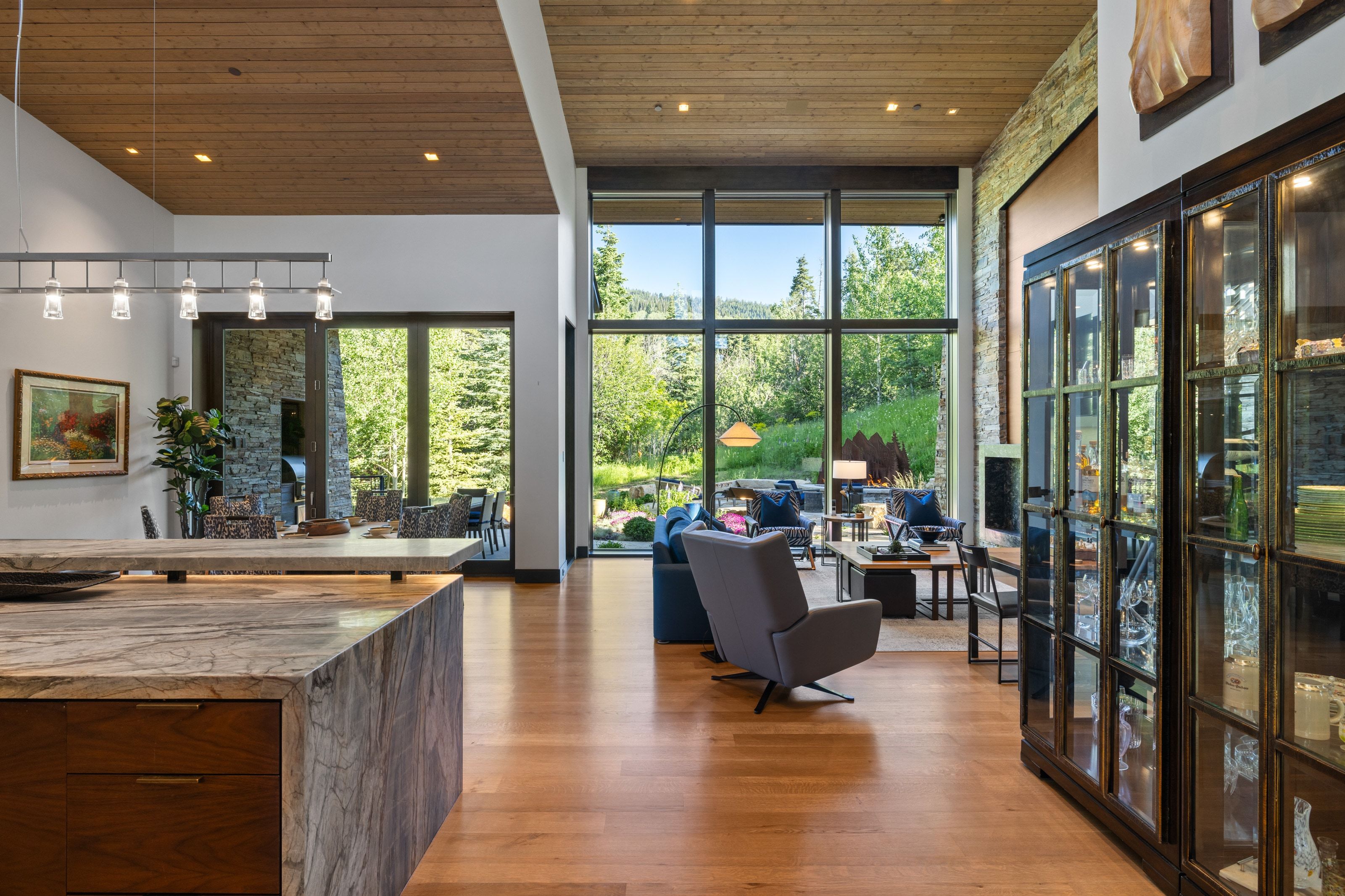 Open-concept living space featuring high ceilings with wood-finish paneling, expansive floor-to-ceiling windows, and hardwood flooring