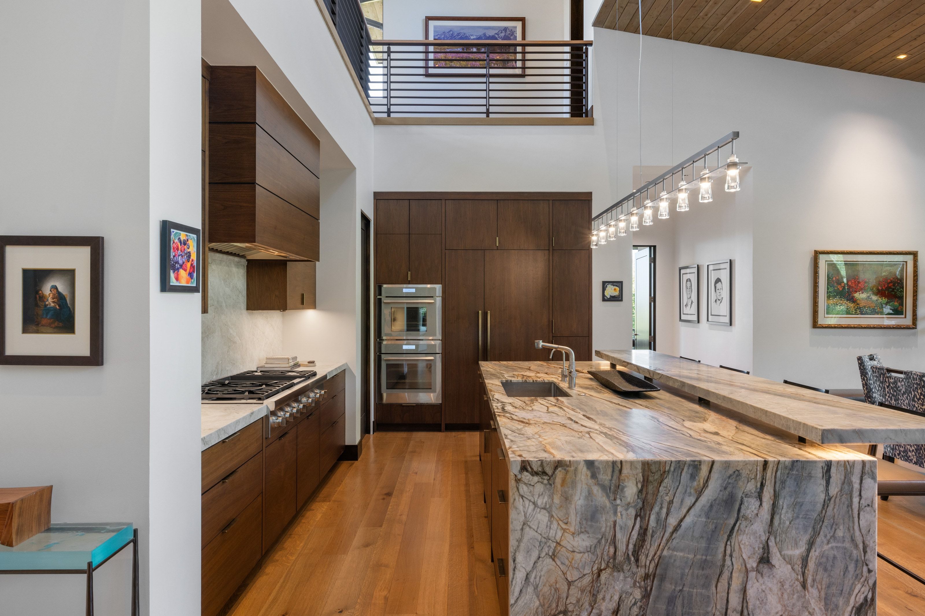 Kitchen featuring a large natural stone island with integrated sink, wood-finish flooring, two-tone cabinetry, and stainless steel double ovens