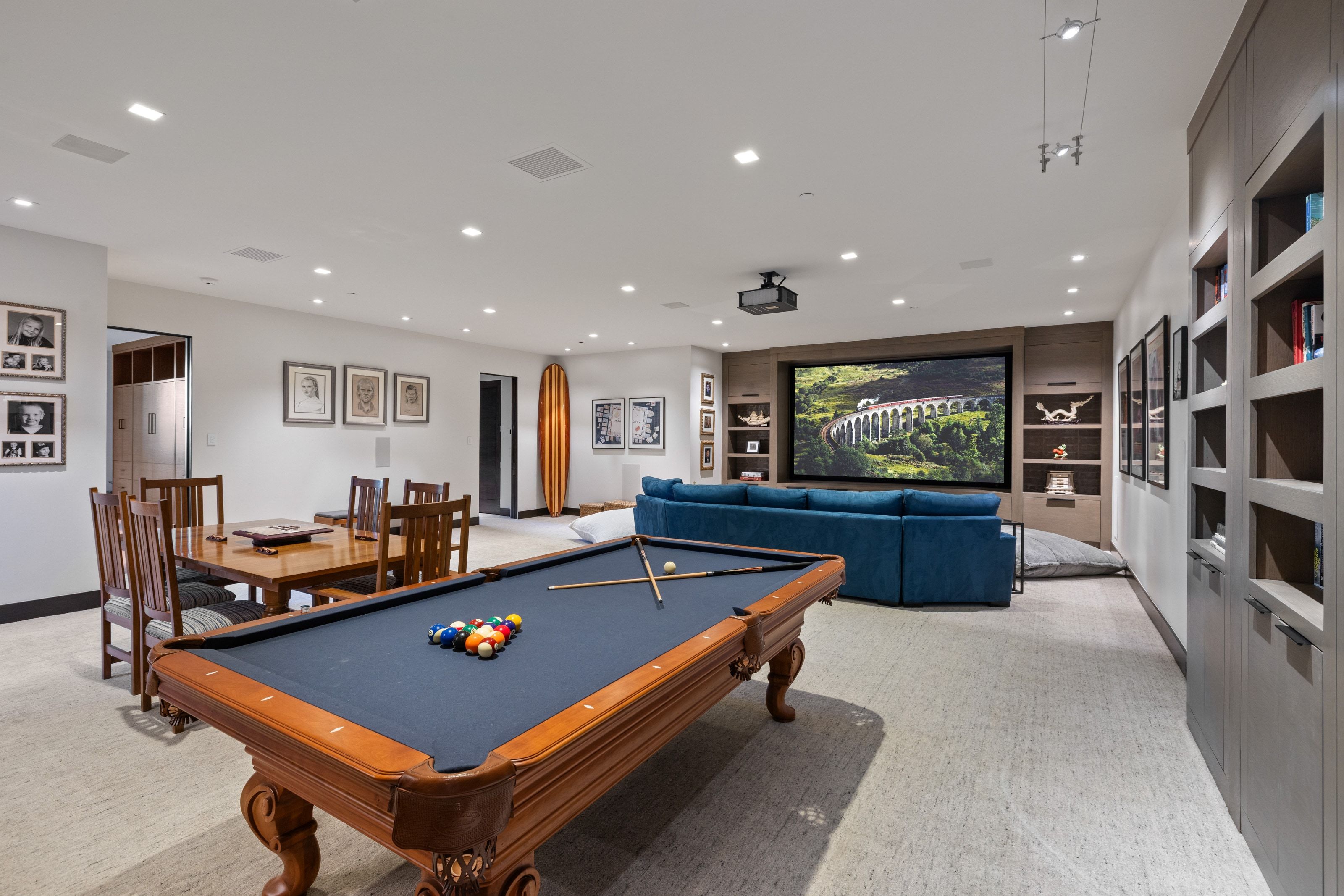 Entertainment space featuring recessed lighting, a built-in media center with shelving, a large projection screen, and integrated ceiling speakers