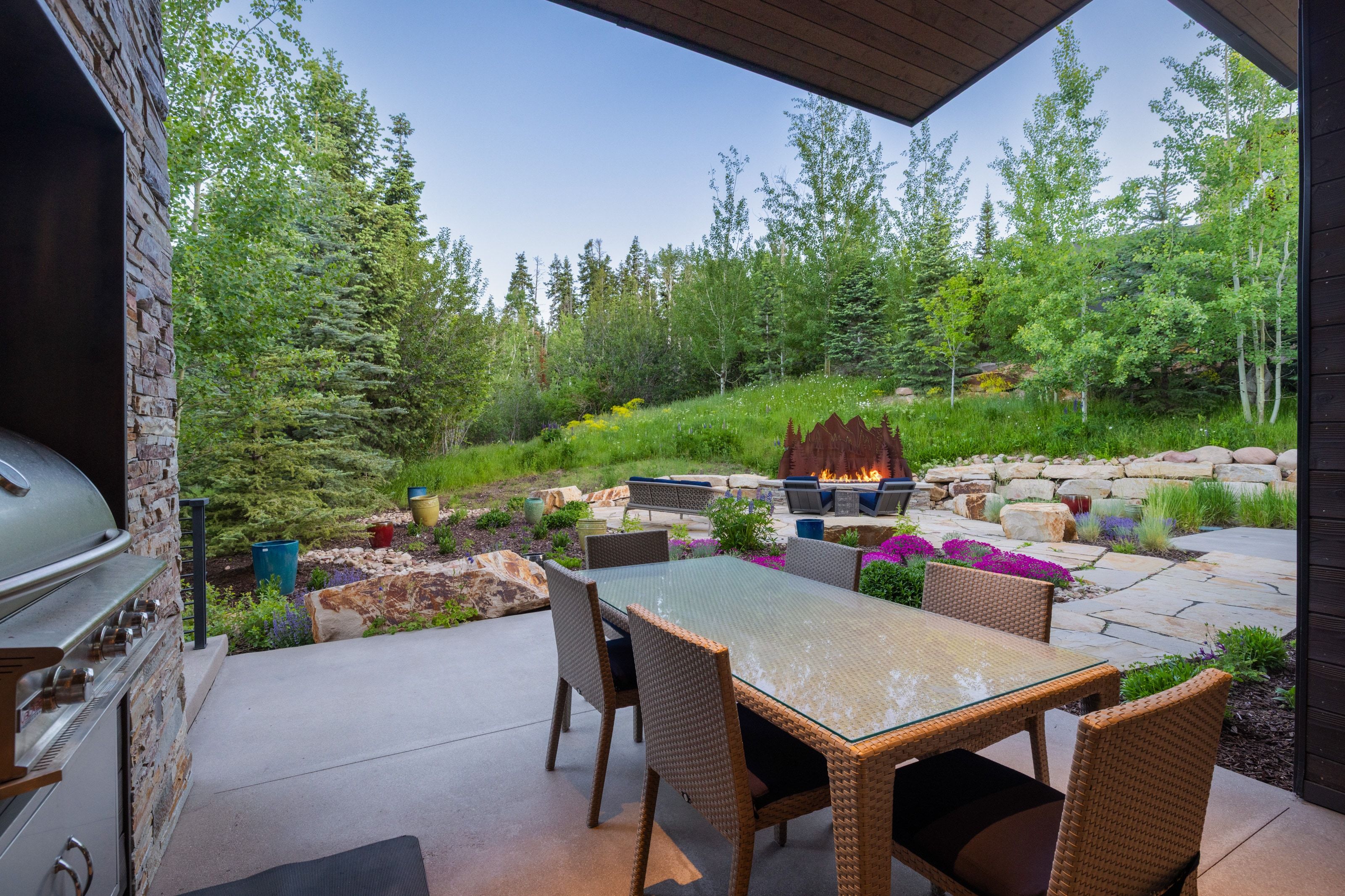 Expansive outdoor living area featuring a built-in stone outdoor kitchen with grill, a concrete patio, and a natural stone patio with a fire feature