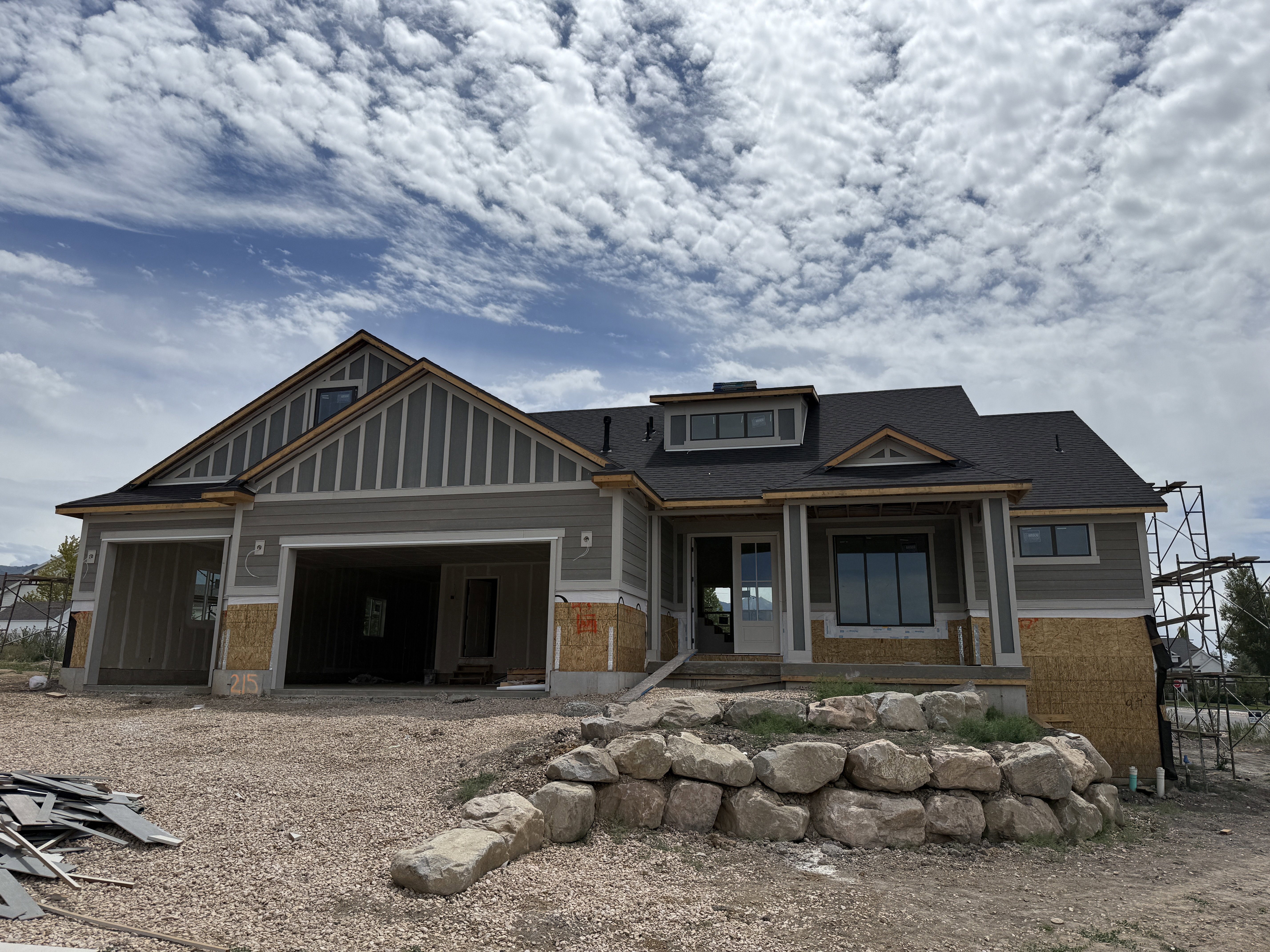 Contemporary exterior featuring gray horizontal siding, dark gray roofing, a front porch, and a stone retaining wall