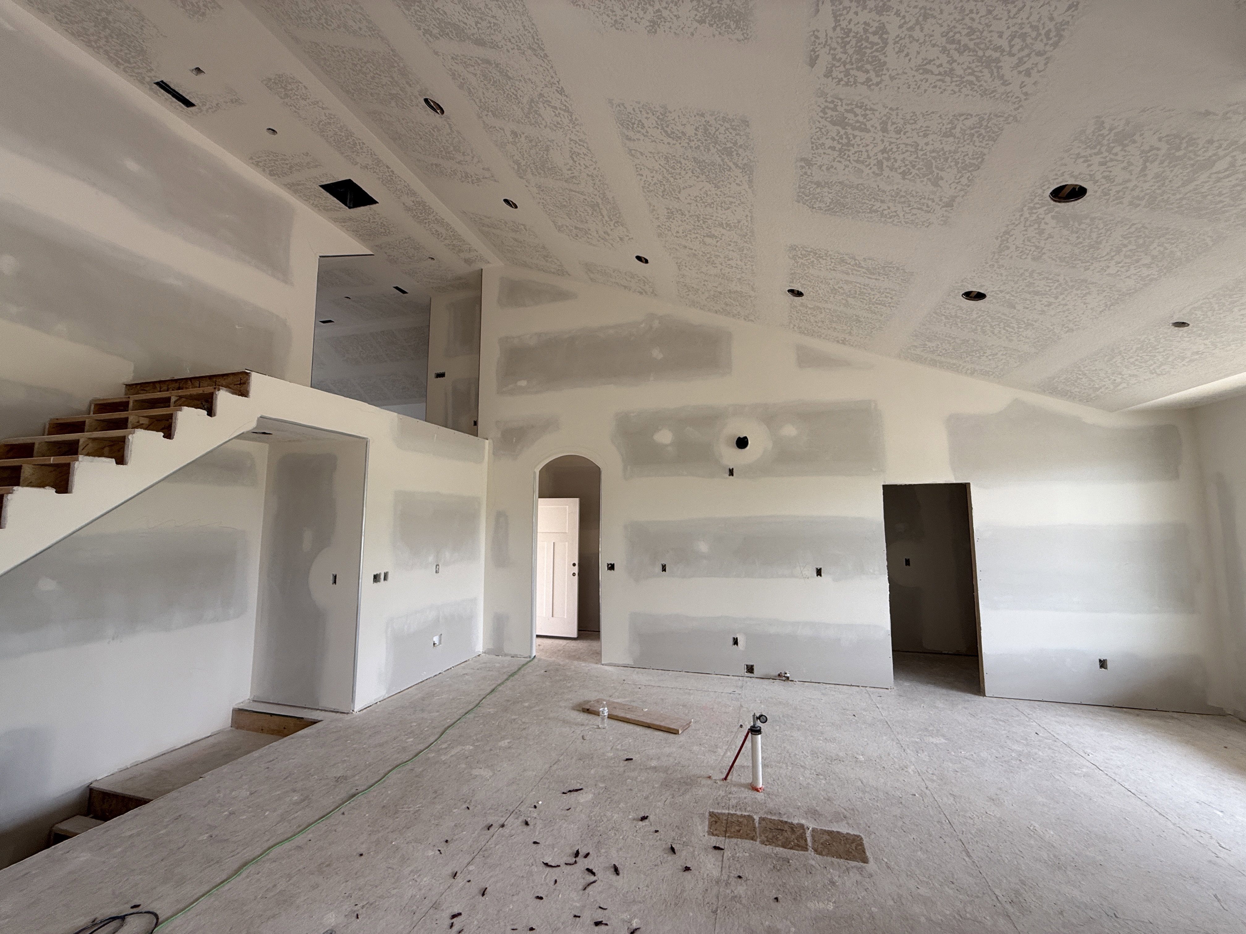 Spacious interior with vaulted ceilings, recessed lighting, an exposed wood staircase, an arched entryway, and multiple doorway openings