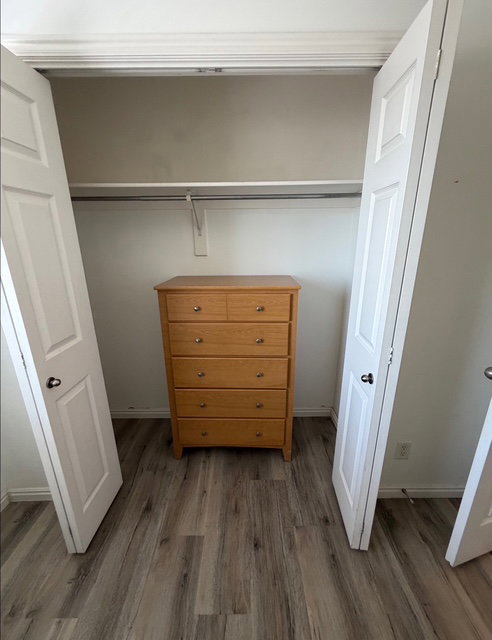 Closet space featuring wood-finish flooring, white bi-fold doors, and a built-in hanging rod