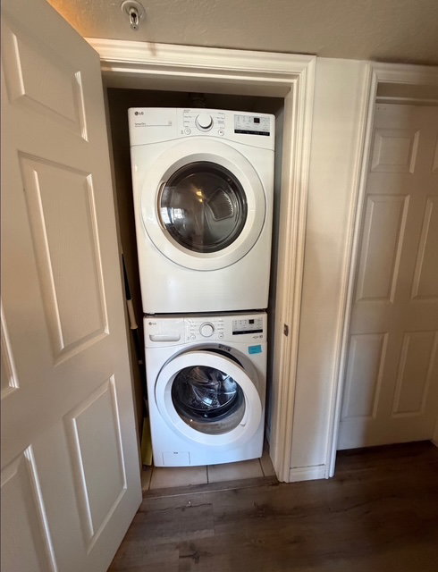 Dedicated laundry closet featuring a stacked white front-loading washer and dryer, tile flooring within the closet, and wood-finish flooring extending into the room