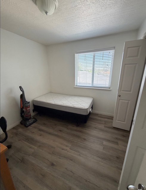 Room featuring wood-finish flooring, a window with blinds, and white walls