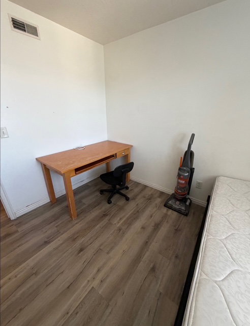 Room featuring wood-finish flooring, white walls, and a ceiling-mounted air vent