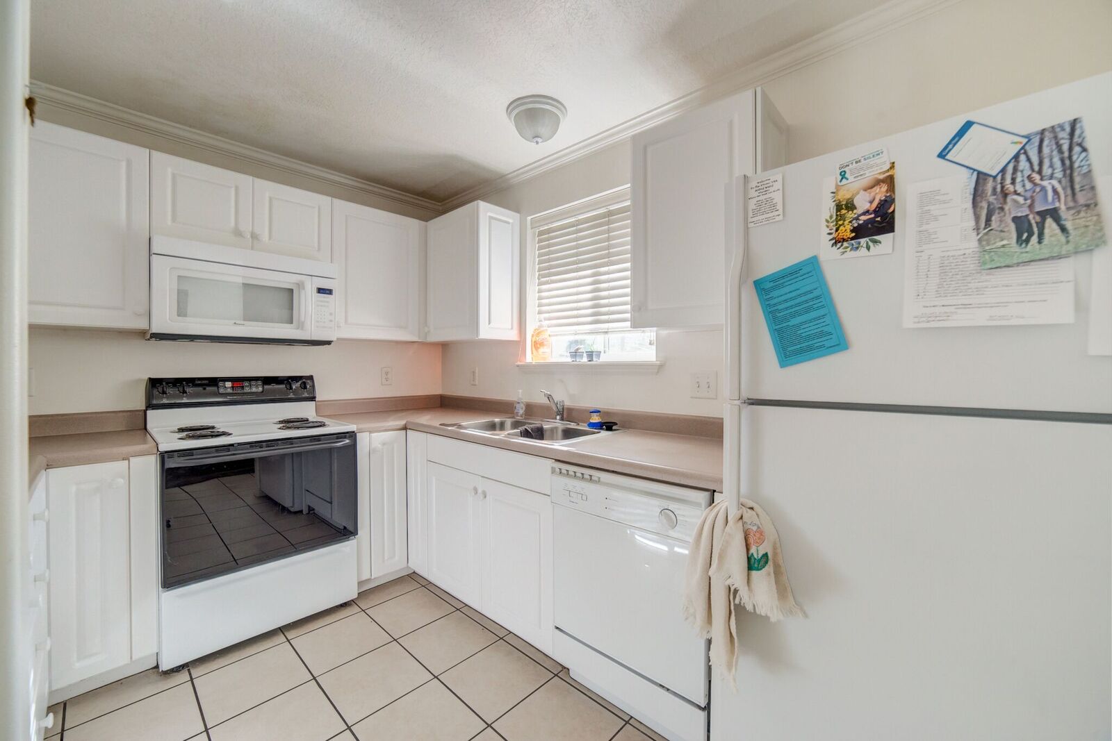 Kitchen featuring white cabinetry, an over-the-range microwave, a white electric range, a double basin sink, and tile flooring