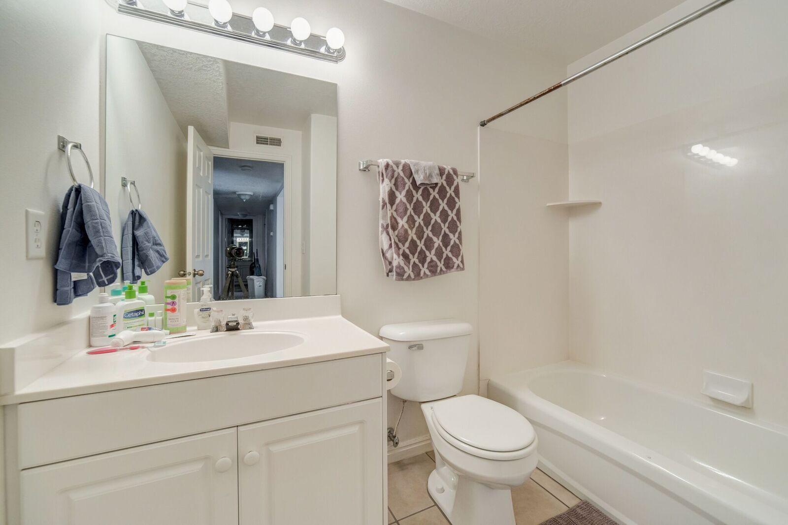 Full bathroom featuring a single vanity with storage, an integrated sink, a rectangular mirror, a four-light vanity fixture, and a combination tub and shower