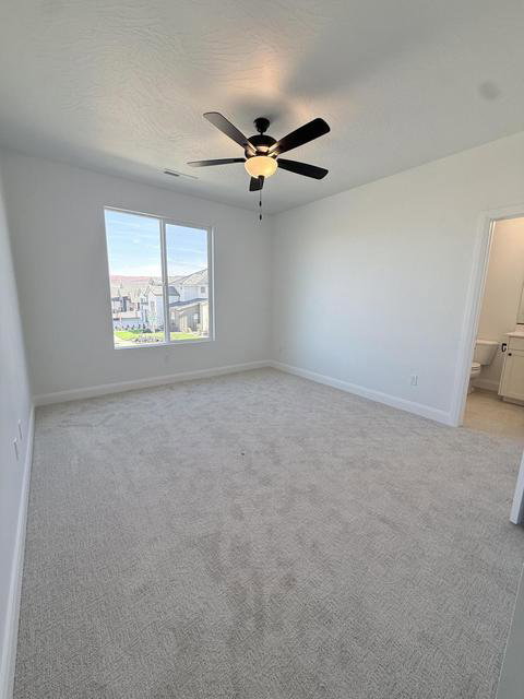 Spacious room featuring neutral carpeting, a large window, a ceiling fan with integrated lighting, and white baseboards