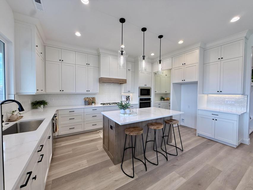 Bright kitchen featuring extensive white cabinetry with matte black hardware, light wood-finish flooring, a central island with a solid surface countertop, and a built-in oven and microwave