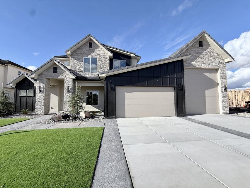 Contemporary residence featuring a light-toned stone and dark vertical siding exterior with gabled rooflines, an attached two-car garage, and a concrete driveway