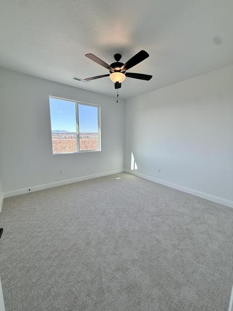 Spacious room featuring light gray carpeting, crisp white walls, a dual-pane window, white baseboards, and a ceiling fan with integrated lighting