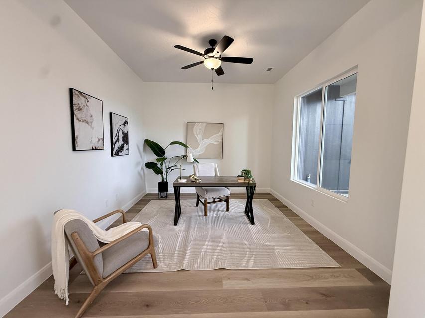 Room featuring light wood-finish flooring, a large window, a ceiling fan with light fixture, and white baseboards