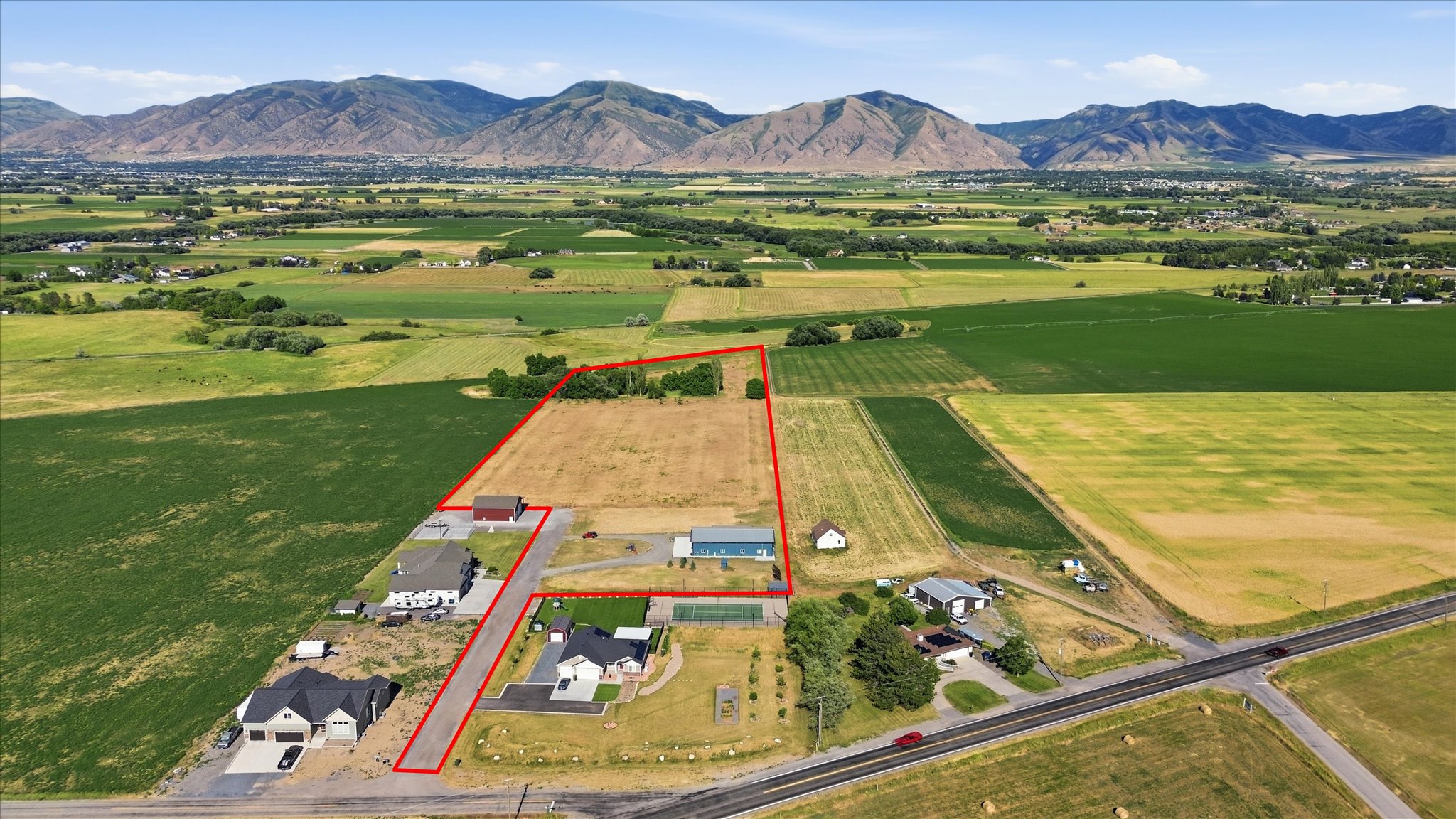 Expansive land parcel featuring existing residential structures, agricultural fields, and mountainous terrain in the background