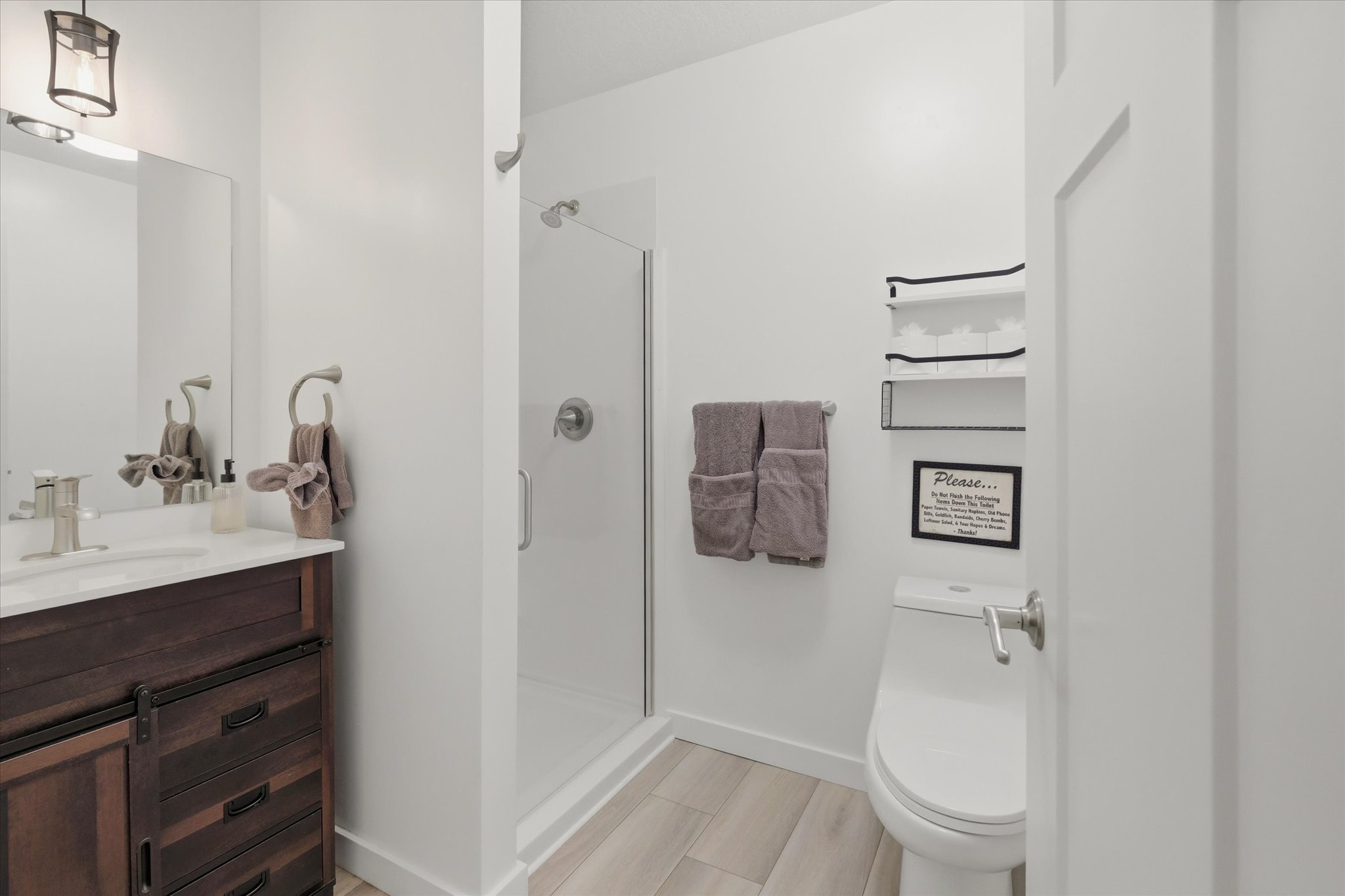 Contemporary bathroom featuring a dark wood-finish vanity with a white countertop, a walk-in shower with a glass enclosure, and light wood-finish flooring