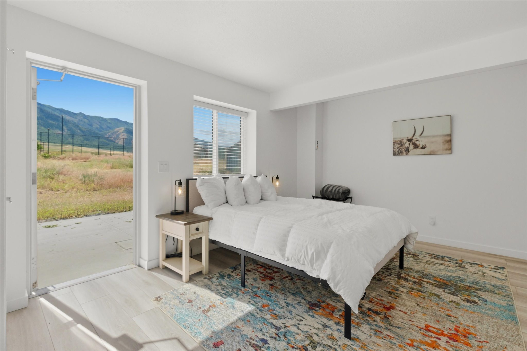 Bedroom featuring a large open doorway to an outdoor patio with mountain scenery, a window with horizontal blinds, and light wood-finish flooring