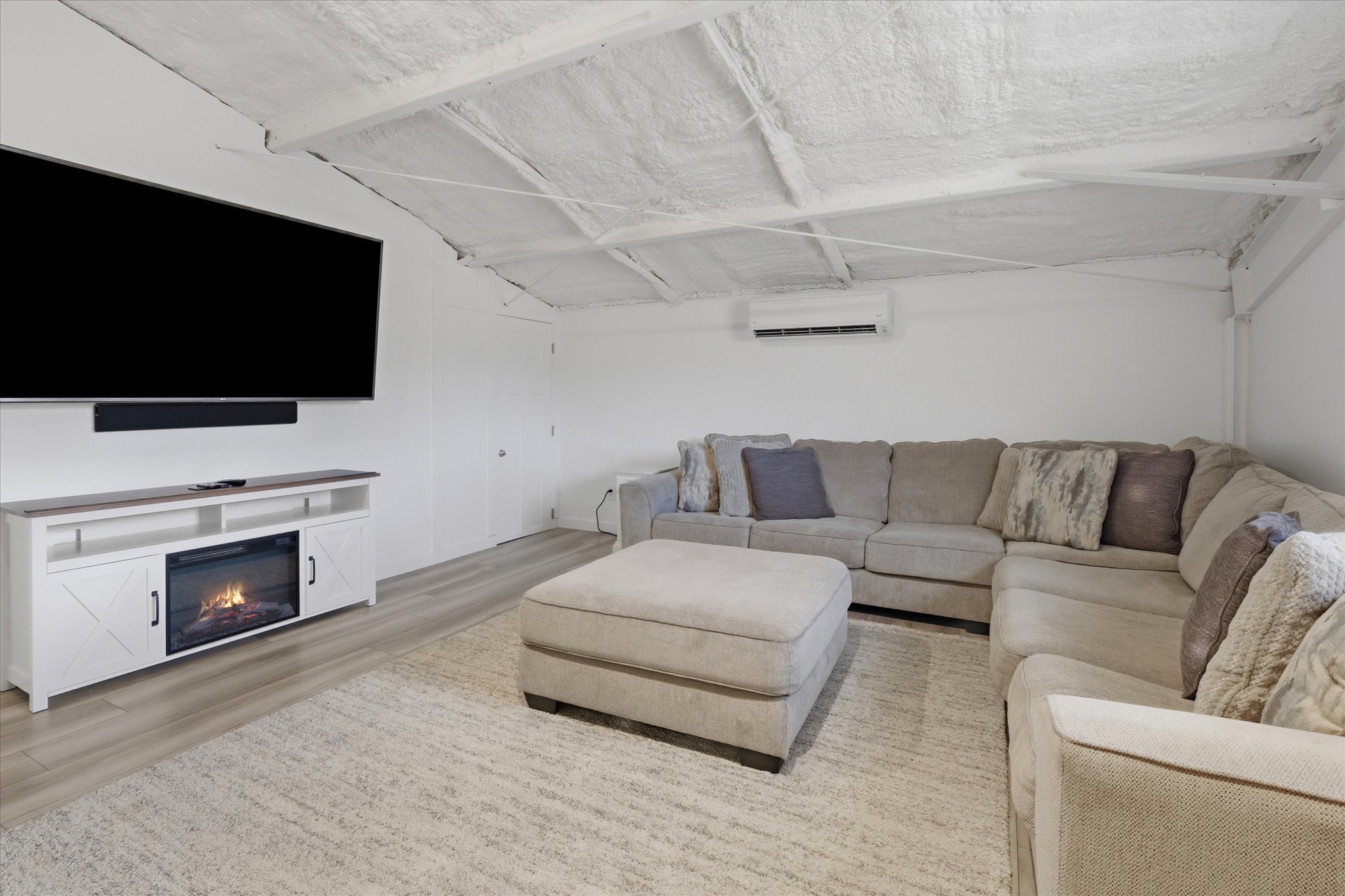 Spacious room featuring a wall-mounted television, a built-in electric fireplace, wood-finish flooring, and white walls
