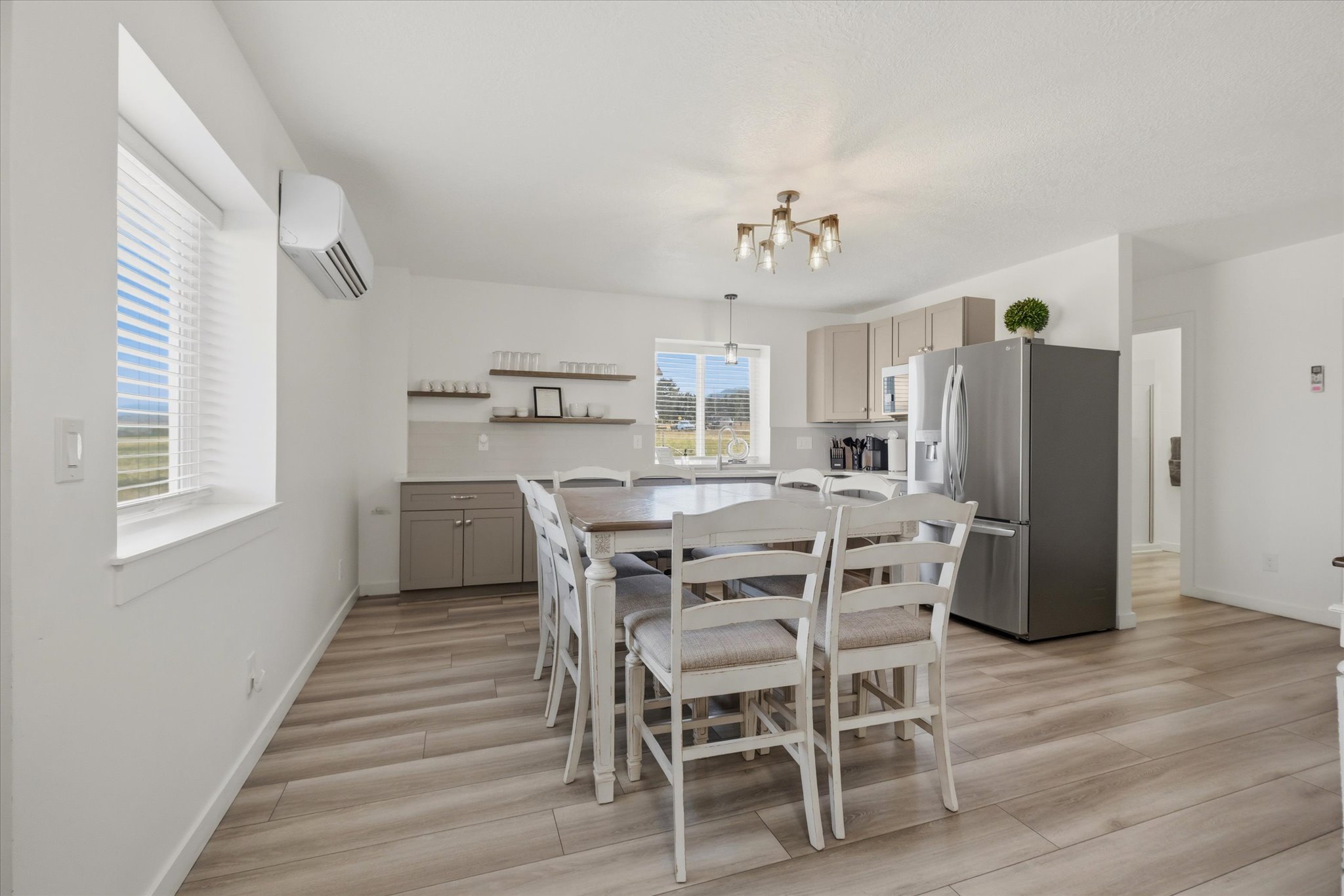 Open-concept living space with wood-finish flooring, a contemporary ceiling light fixture, a stainless steel refrigerator, and ample natural light from multiple windows