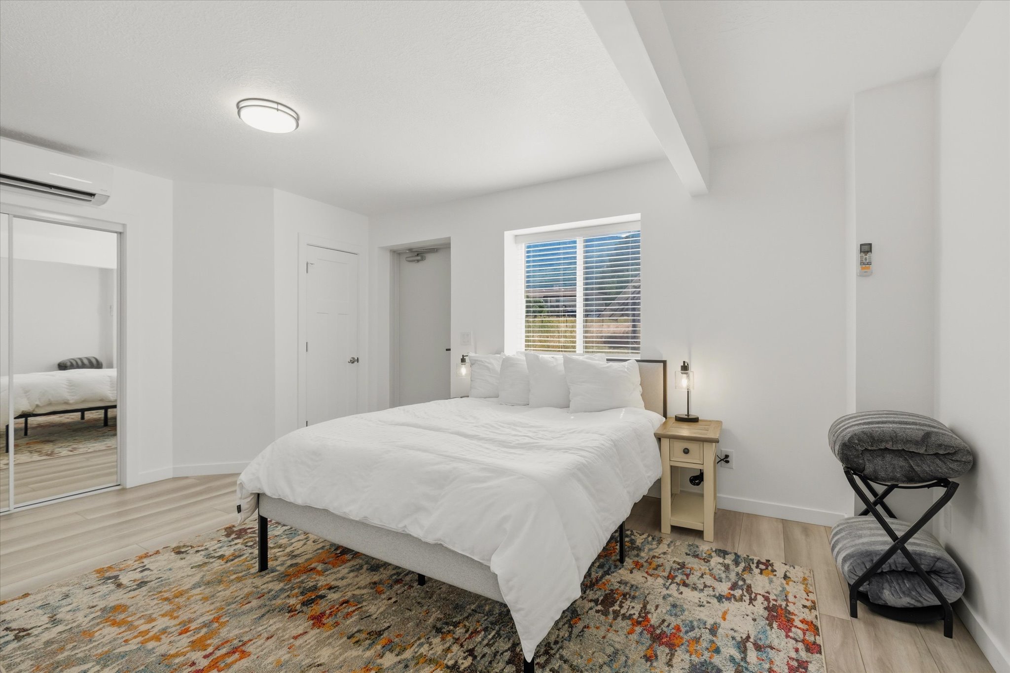 Bright interior space featuring light wood-finish flooring, a window with blinds, and a built-in air conditioning unit