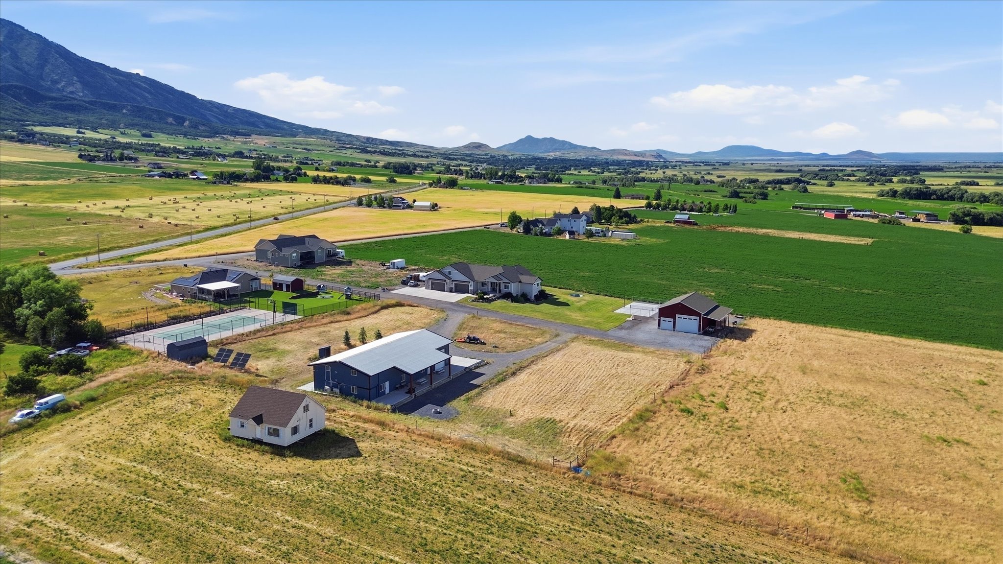 Expansive rural property featuring a tennis court, a modern barn-style structure with a covered patio, and a detached two-car garage