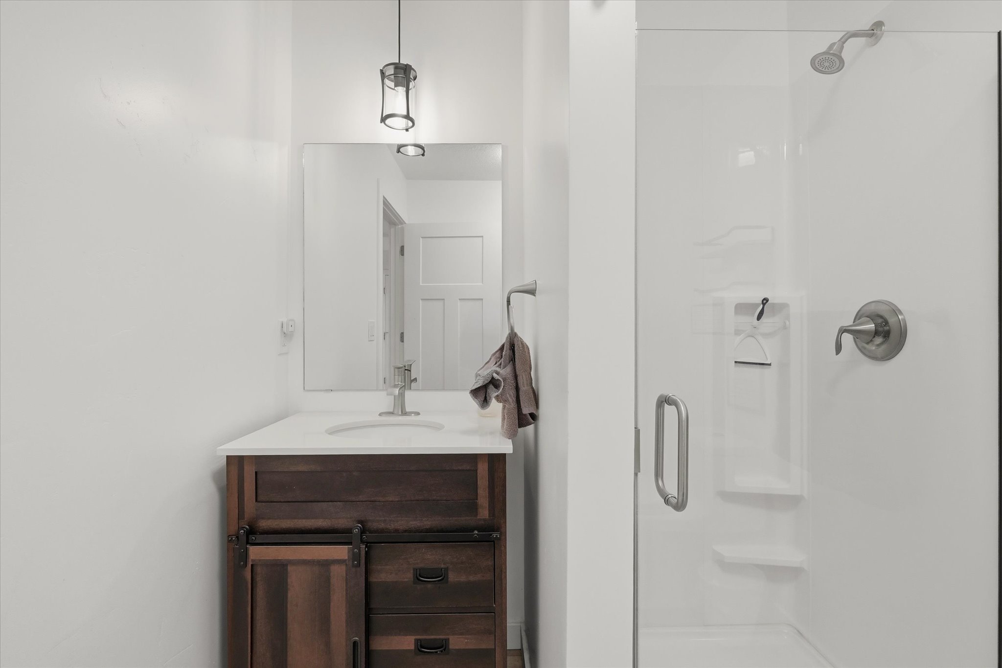 Bathroom featuring a dark wood-finish vanity with a white countertop and undermount sink, brushed nickel faucet, and a glass-enclosed shower with a built-in shelf