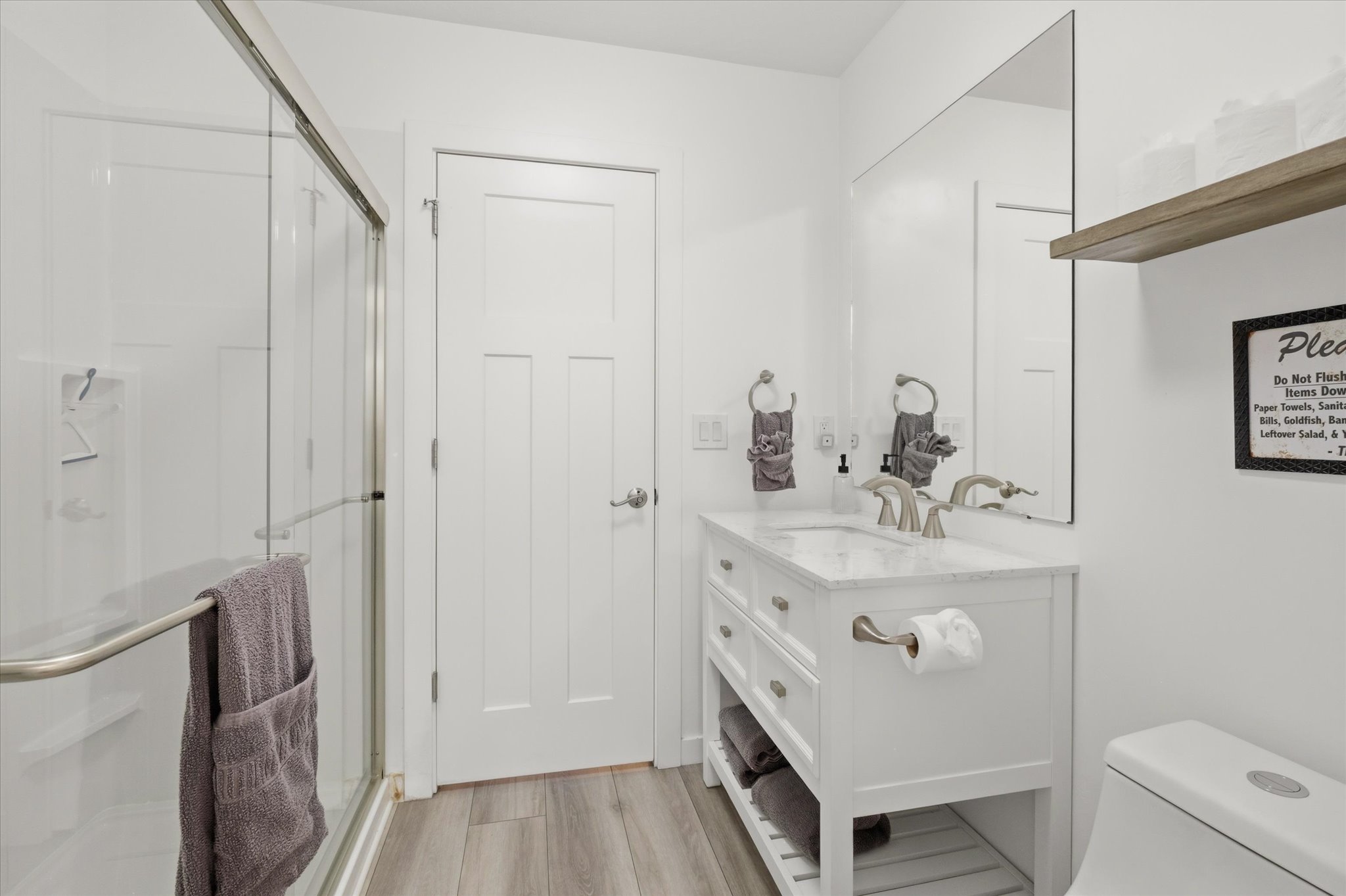 Bright white bathroom featuring a glass-enclosed shower with an integrated shelf, a paneled door, and wood-finish flooring