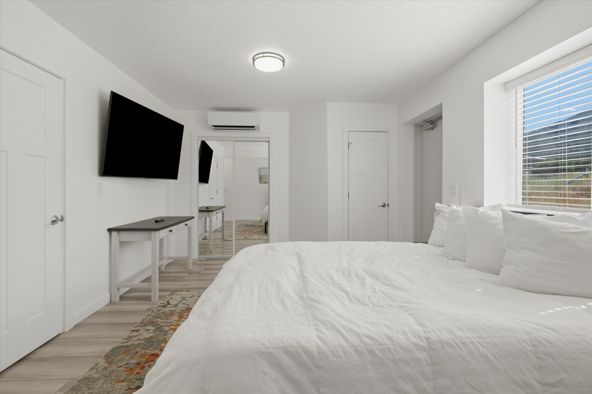 White walls featuring wood-finish flooring, a window with horizontal blinds, and a built-in wall unit