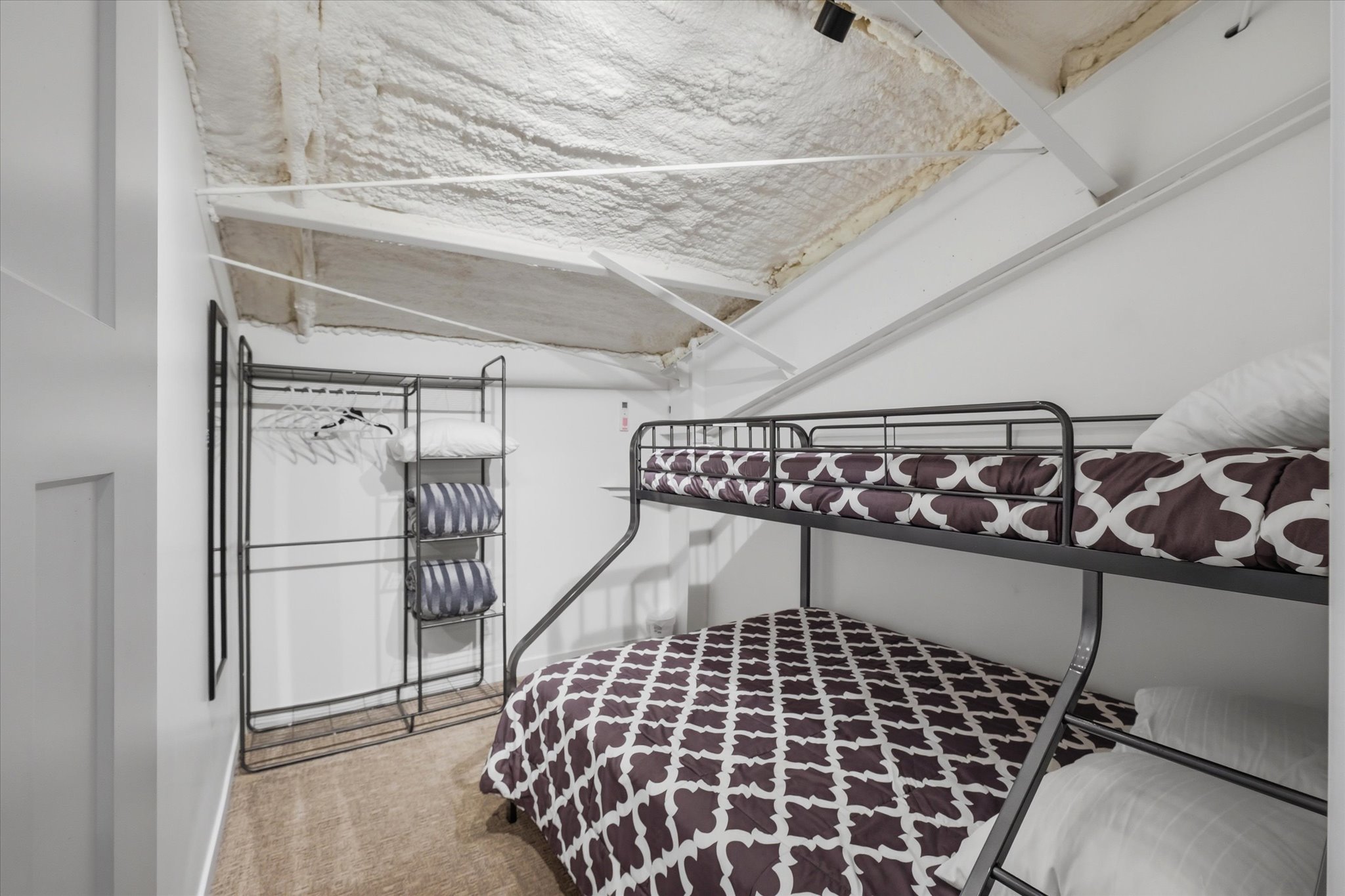 Room featuring an exposed beam ceiling with spray foam insulation, light-colored walls, and carpeting