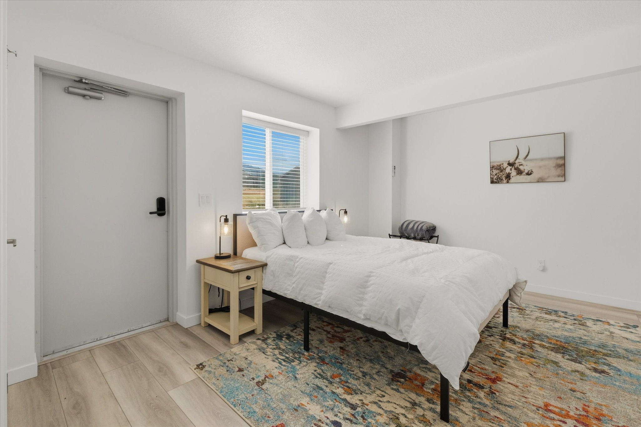 Bedroom featuring light wood-finish flooring, white walls, and a window with horizontal blinds