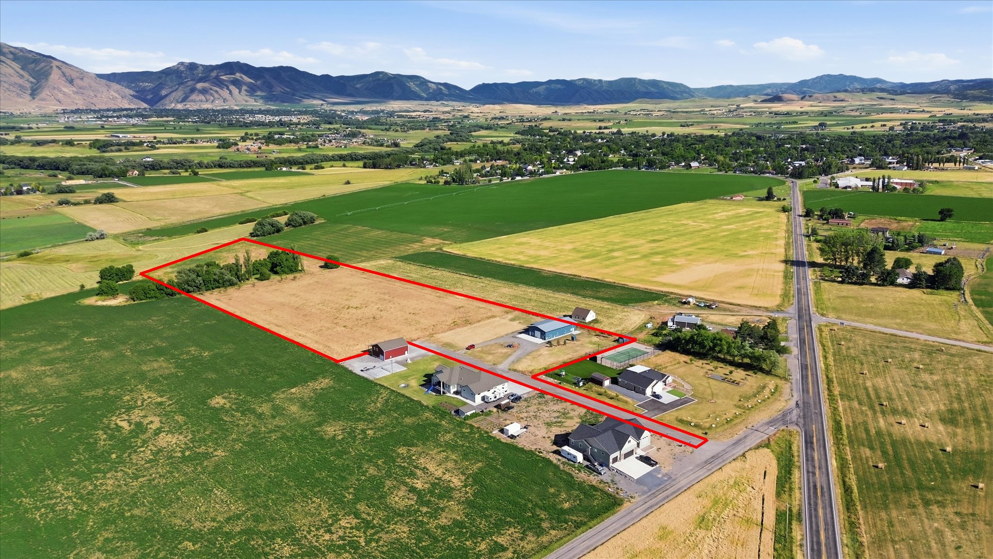 Expansive rural property featuring a large open field, mature trees, and mountainous terrain in the background