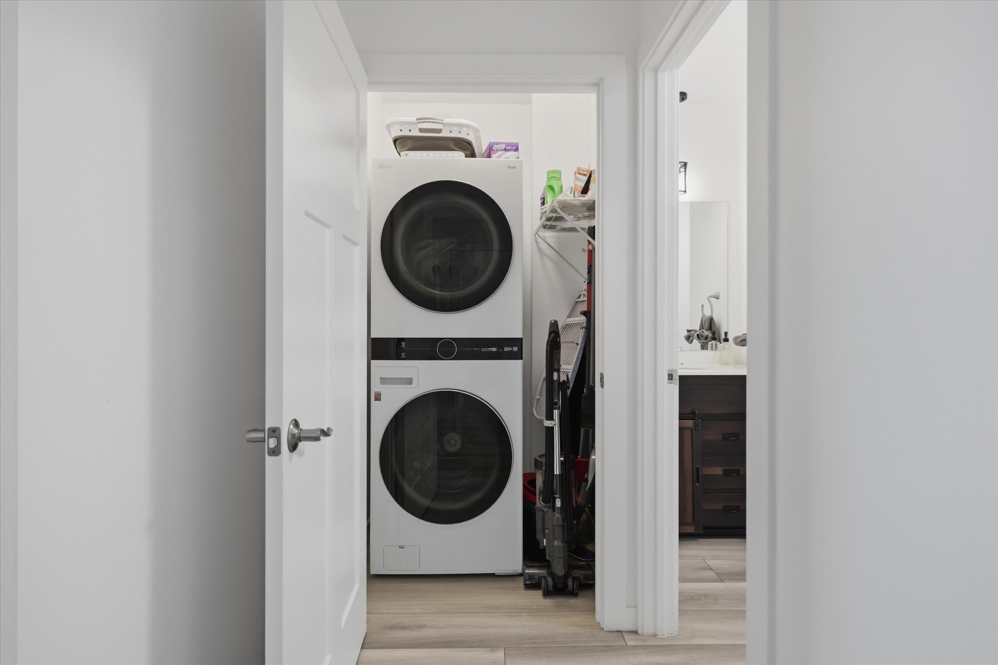 Dedicated laundry area featuring stacked front-loading appliances and light wood-finish flooring