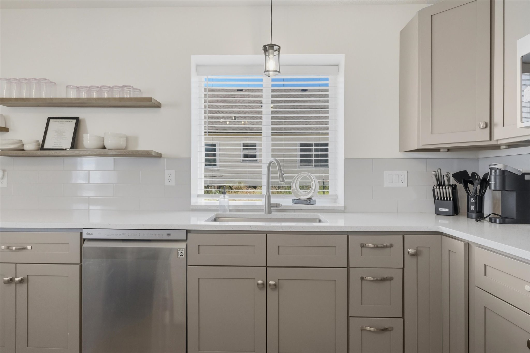 Modern kitchen featuring light gray cabinetry, stainless steel dishwasher, white subway tile backsplash, and light-toned countertops