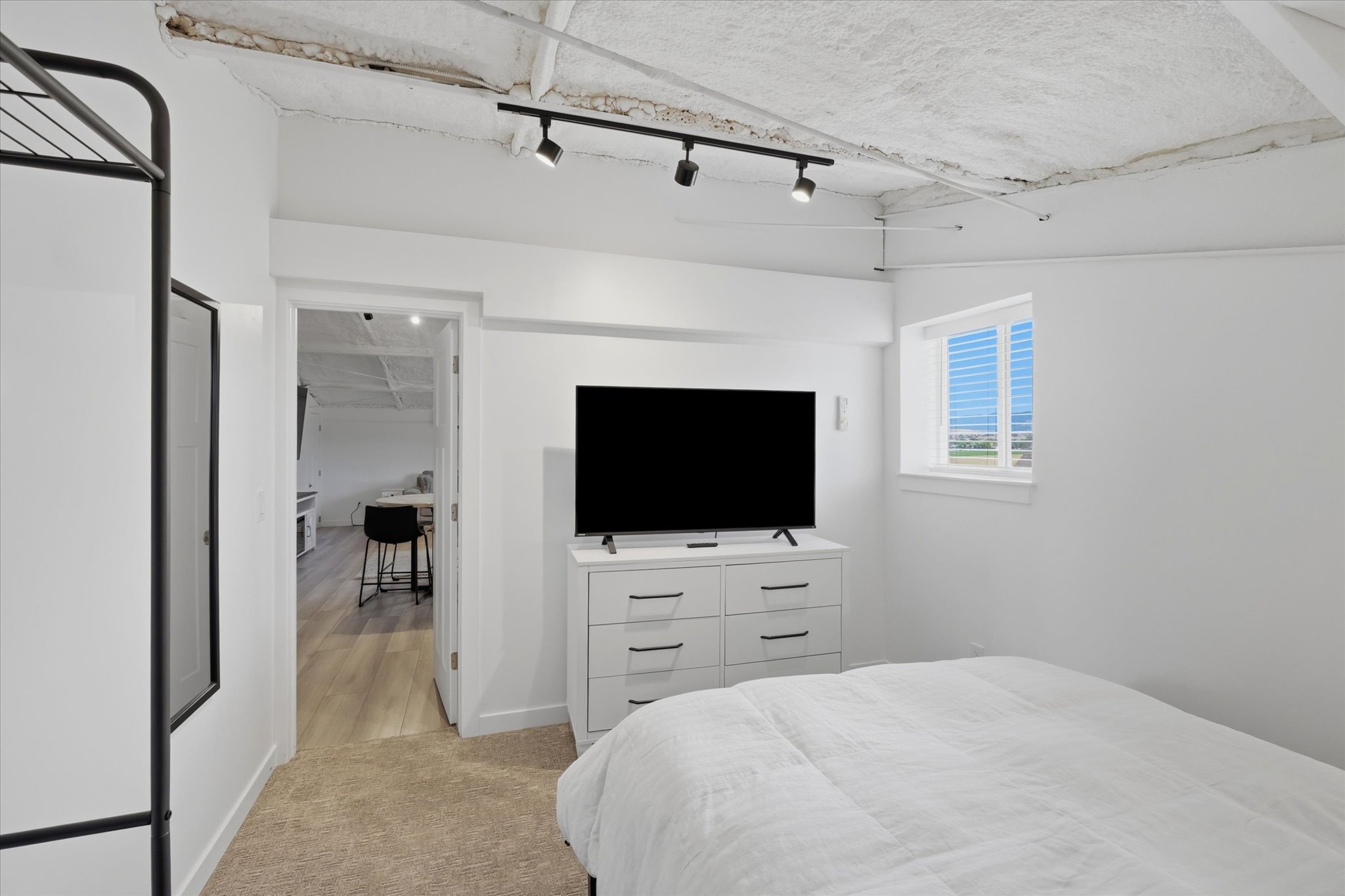 Bedroom featuring track lighting, exposed ceiling texture, white walls, and a window with blinds